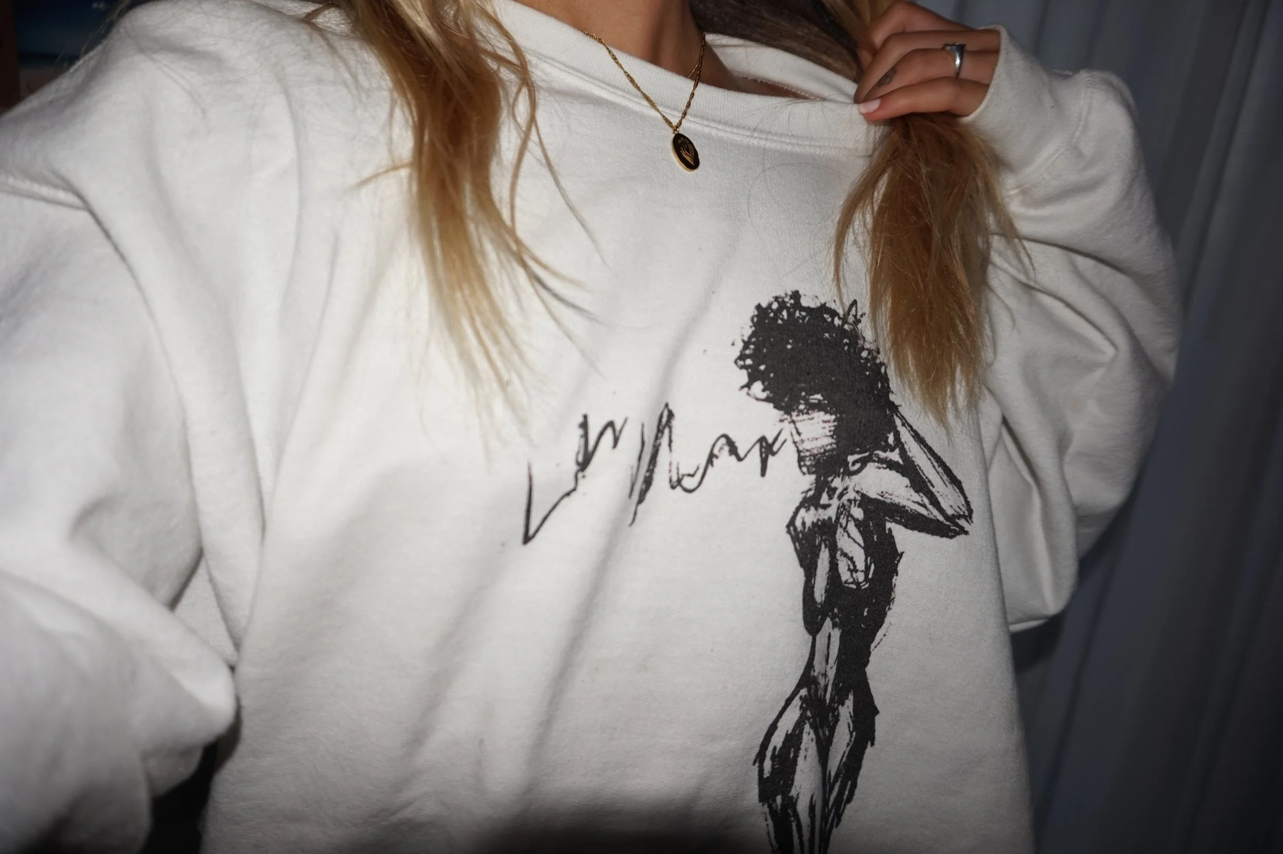 Person wearing a white sweatshirt with an artistic black graphic of a figure and a necklace with a pendant.