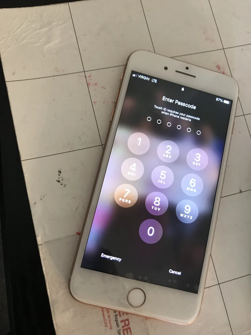 iPhone displaying a passcode entry screen on a white tiled surface