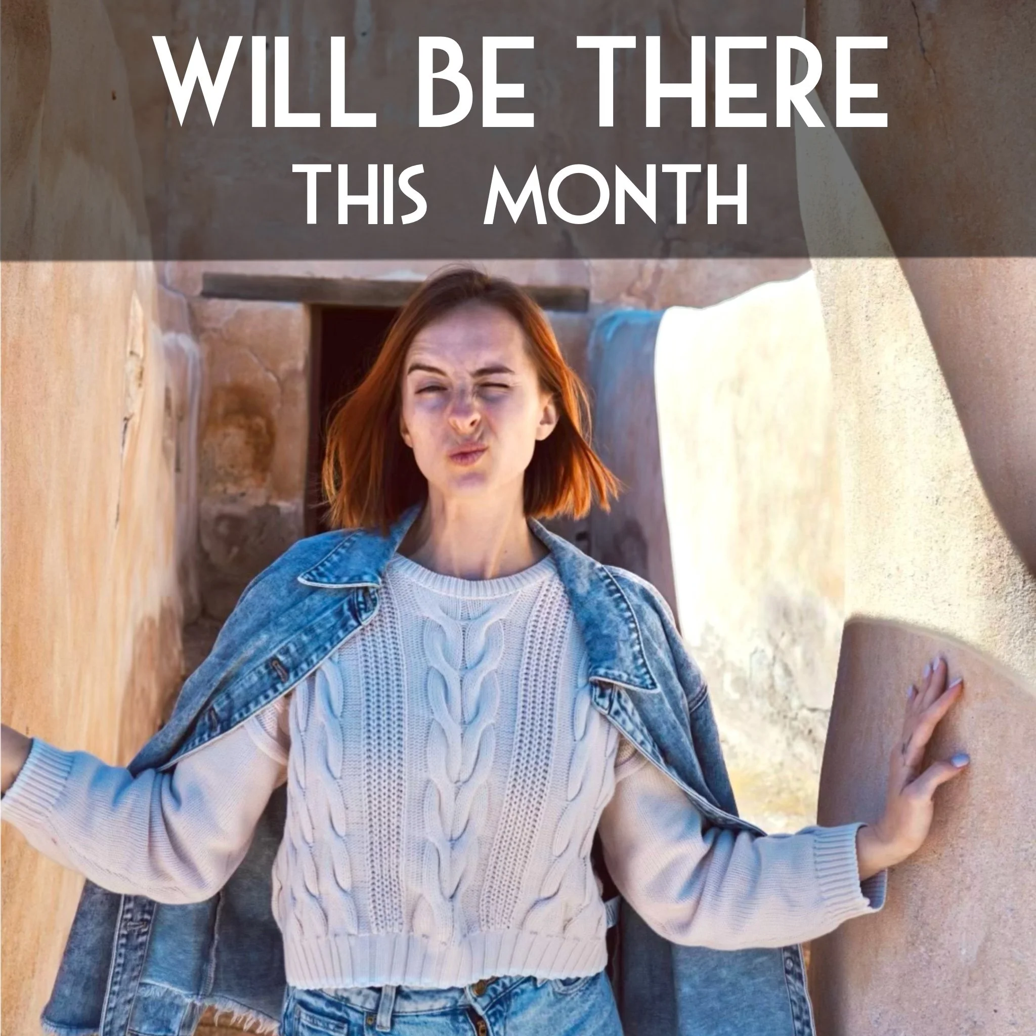 A woman with red hair, wearing a white sweater and denim jacket, making a funny face with her eyes closed and lips puckered. She is leaning against a wooden wall with her arms resting on it.