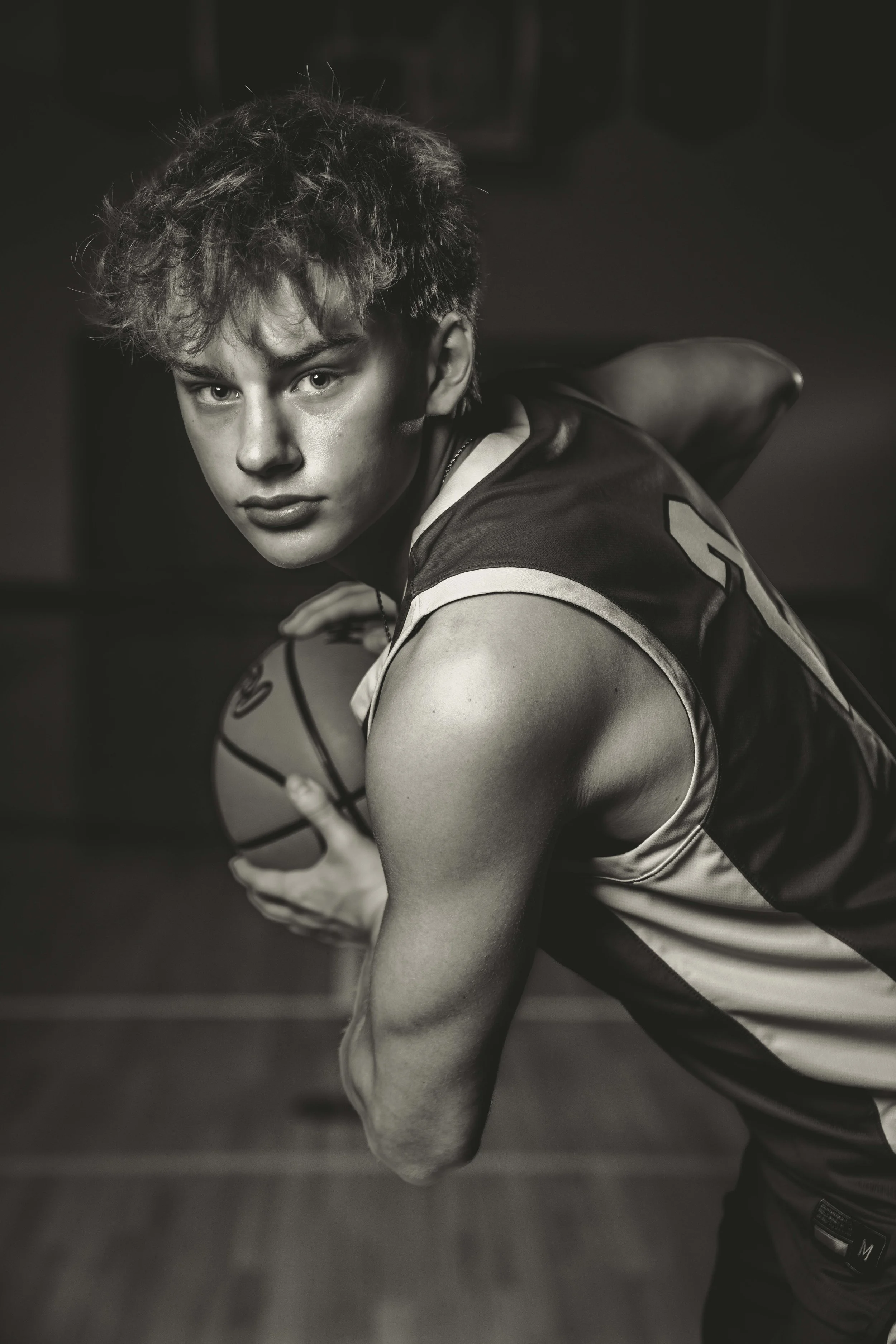 A young man with curly hair and a focused expression holding a basketball in a gym.