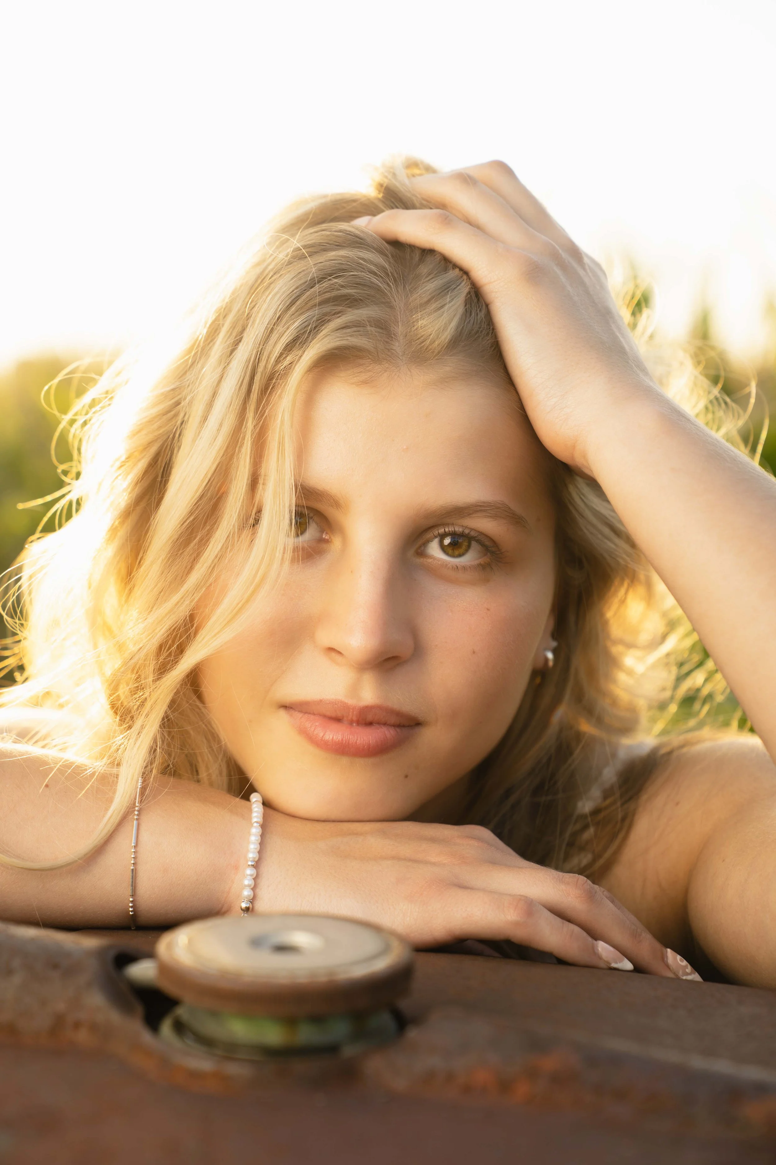 A young woman with blonde hair resting her head on a surface outdoors during sunset, with sunlight illuminating her face.