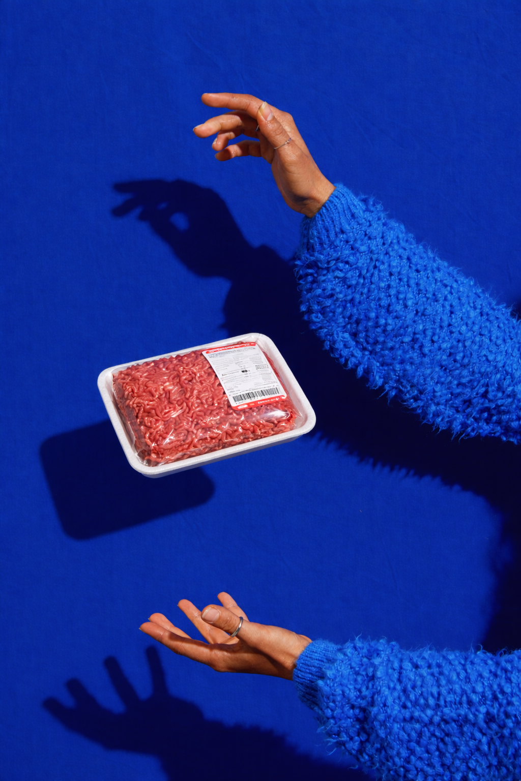 Person wearing a blue fuzzy sweater holding a tray of ground beef against a blue background, casting a shadow.