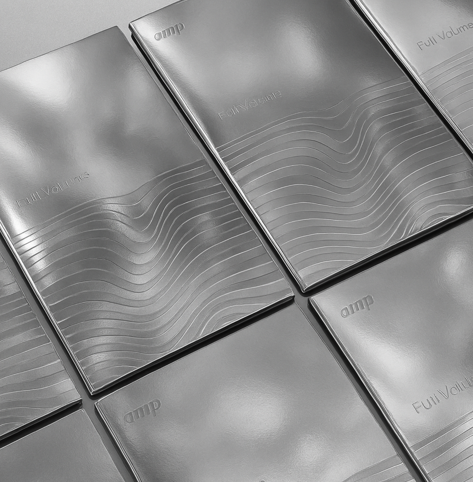 Close-up of metallic portable speakers with embossed wave patterns and the words 'Full Volume' and 'amp' on the surface.