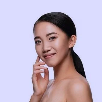 A young woman with long dark hair, smiling, posing with her hand near her face against a light purple background.
