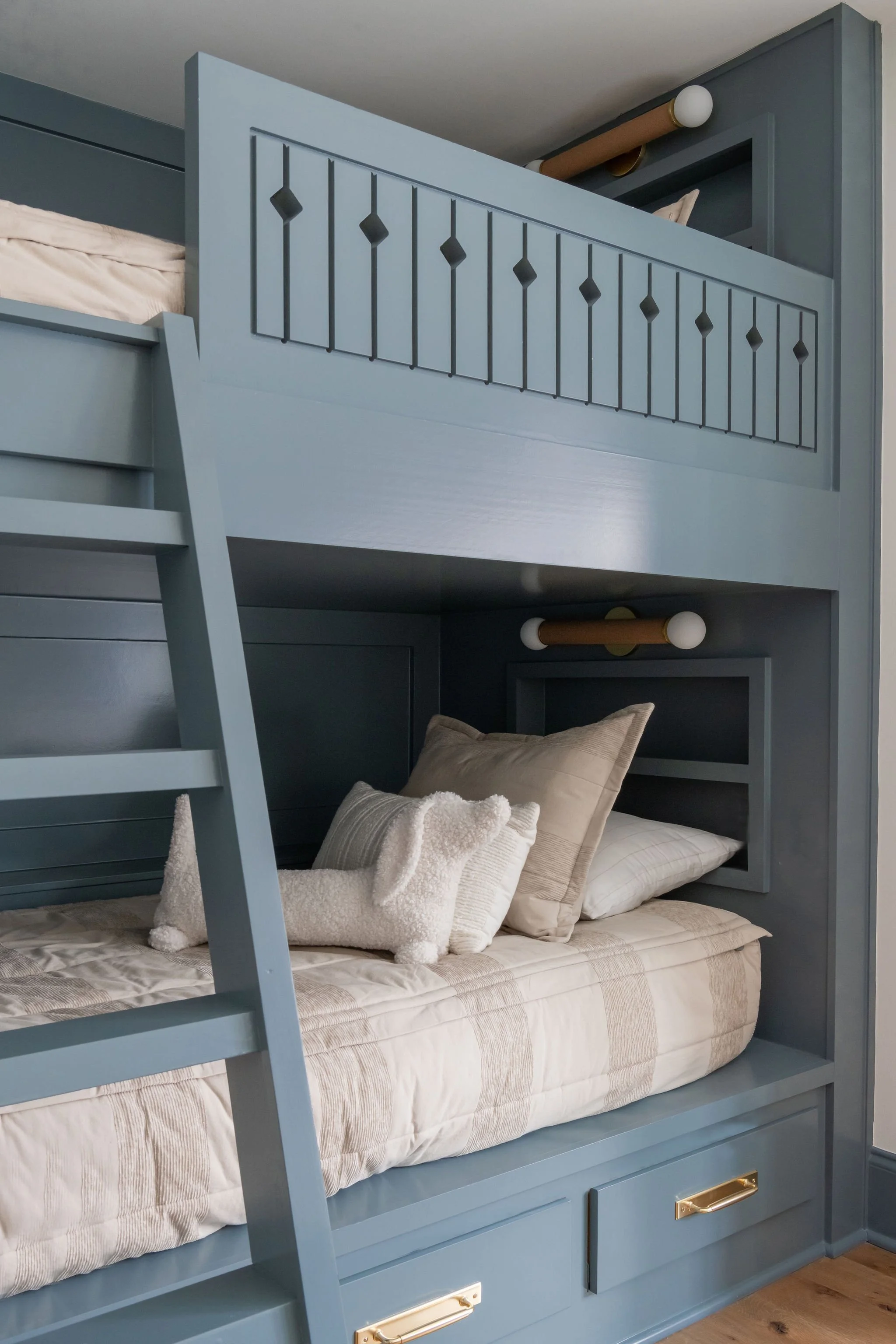 Blue wooden bunk bed with storage drawers, featuring a lower bed with pillows and plush toys, and an upper bunk with a partial view of bedding.