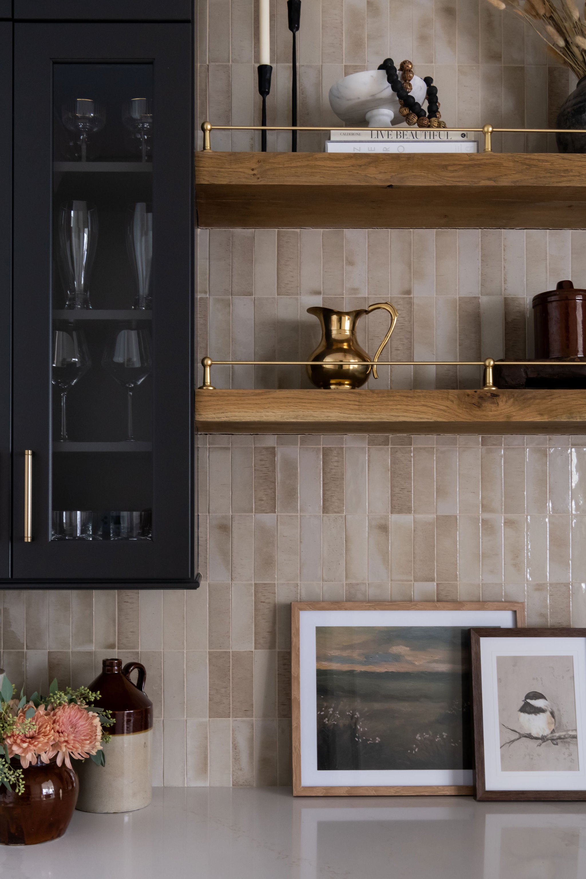 Decorative kitchen corner with two wooden shelves, glassware display cabinet, framed art, flowers, and decorative vases.