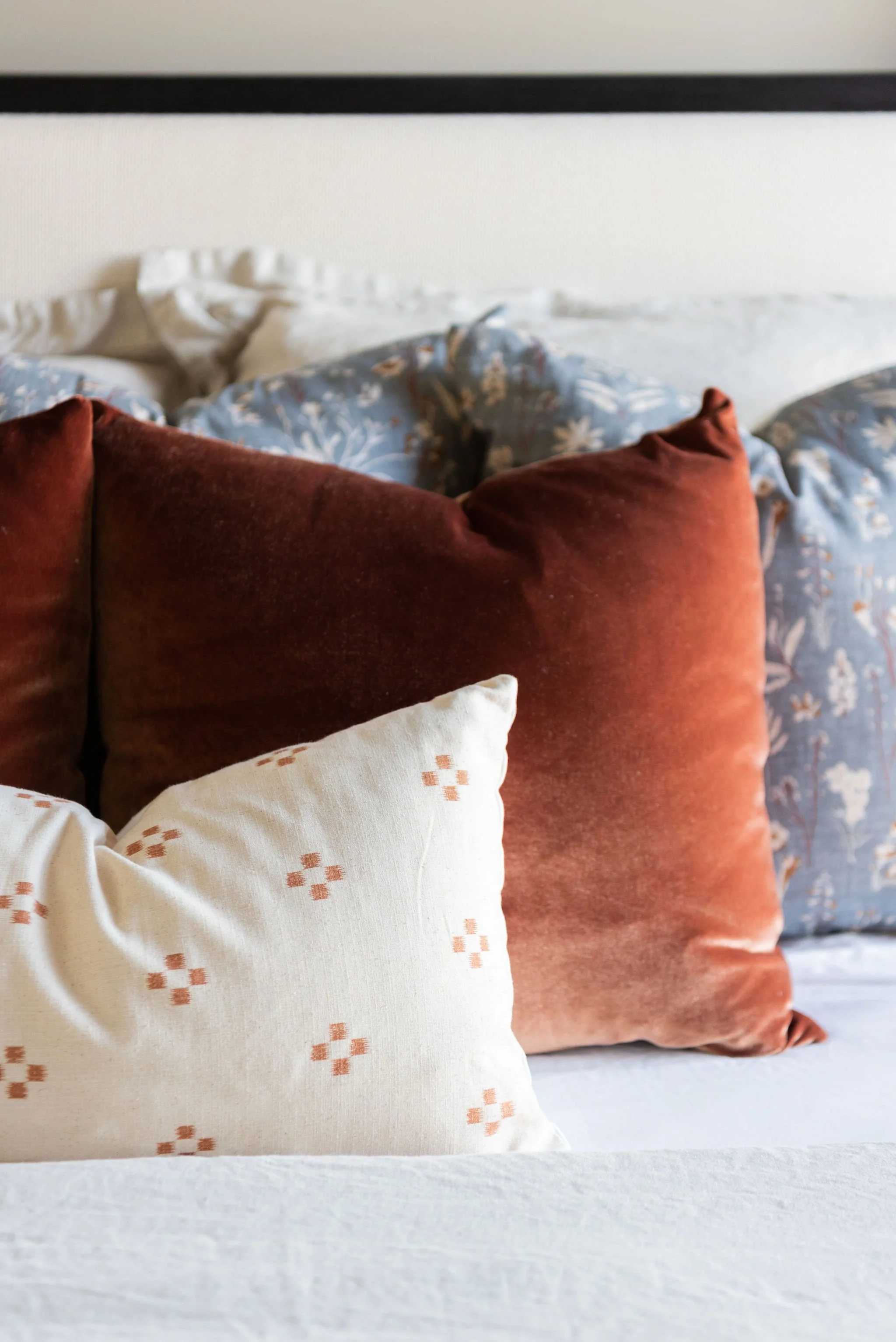 A bed with decorative pillows, including white, rust-colored, and blue floral patterned pillows.