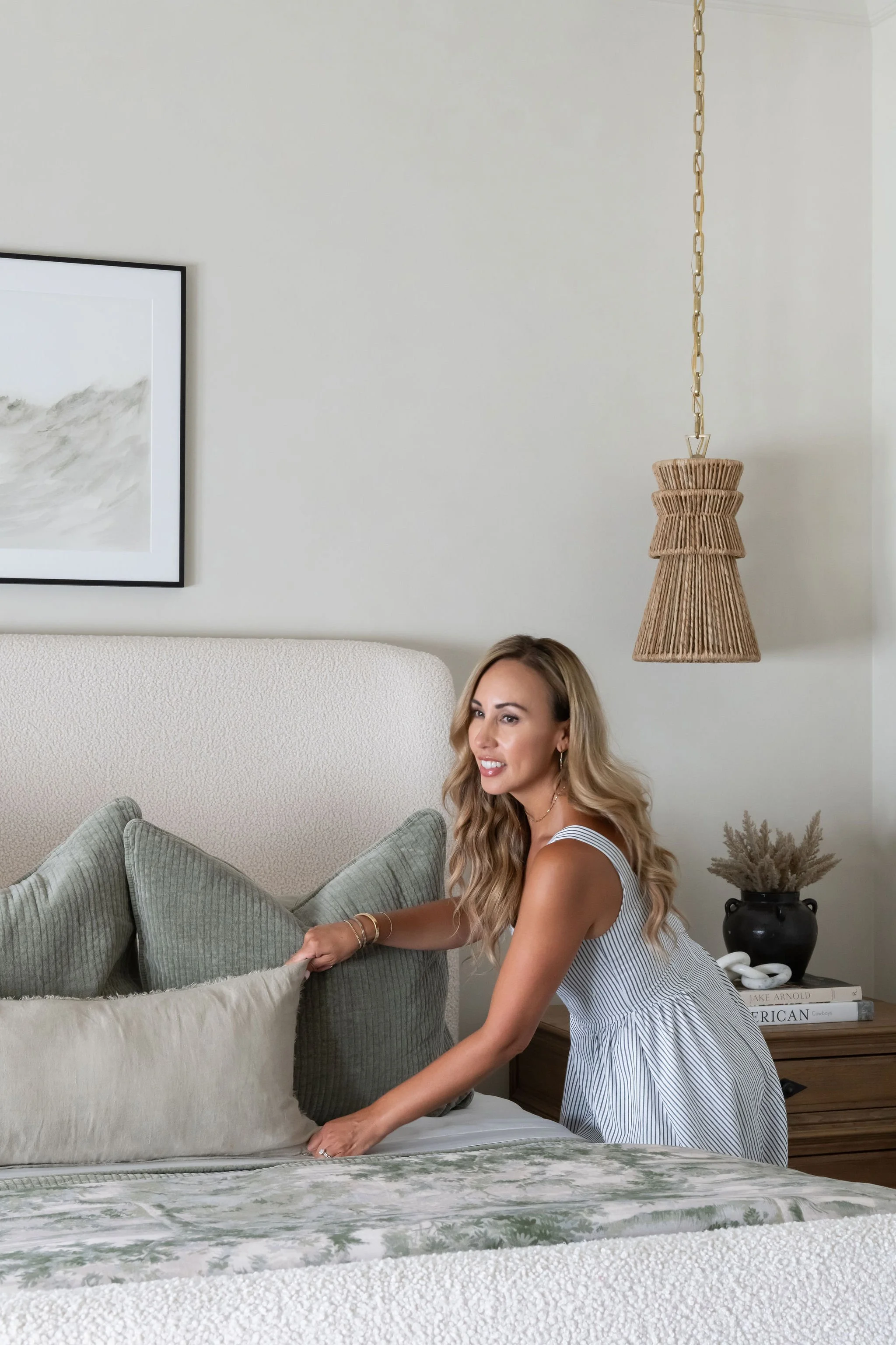 Woman making bed with pillows in a bedroom.