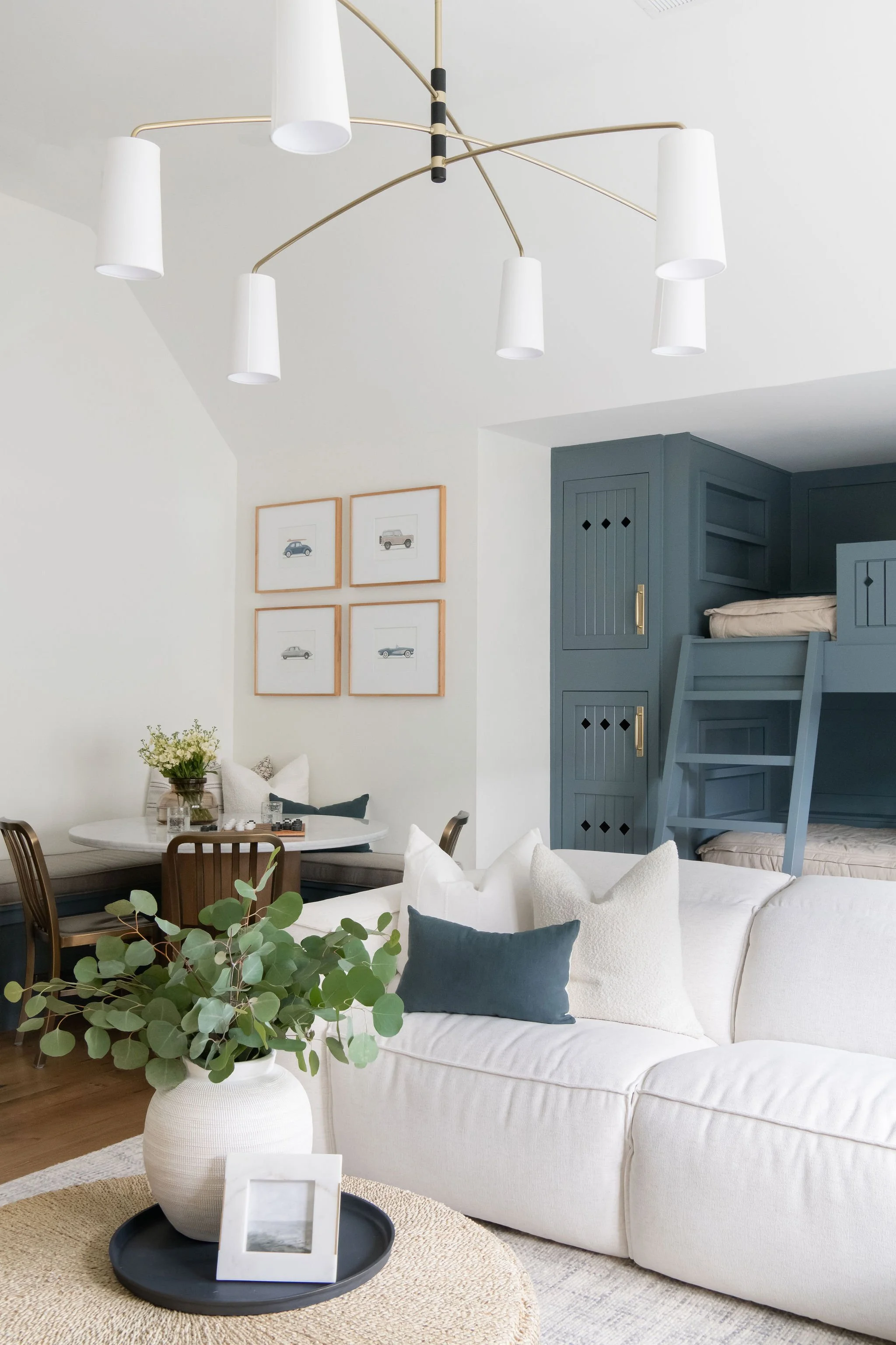Living room with white sofa, green potted plant, round coffee table, blue bunk beds, wall art, and modern chandelier.