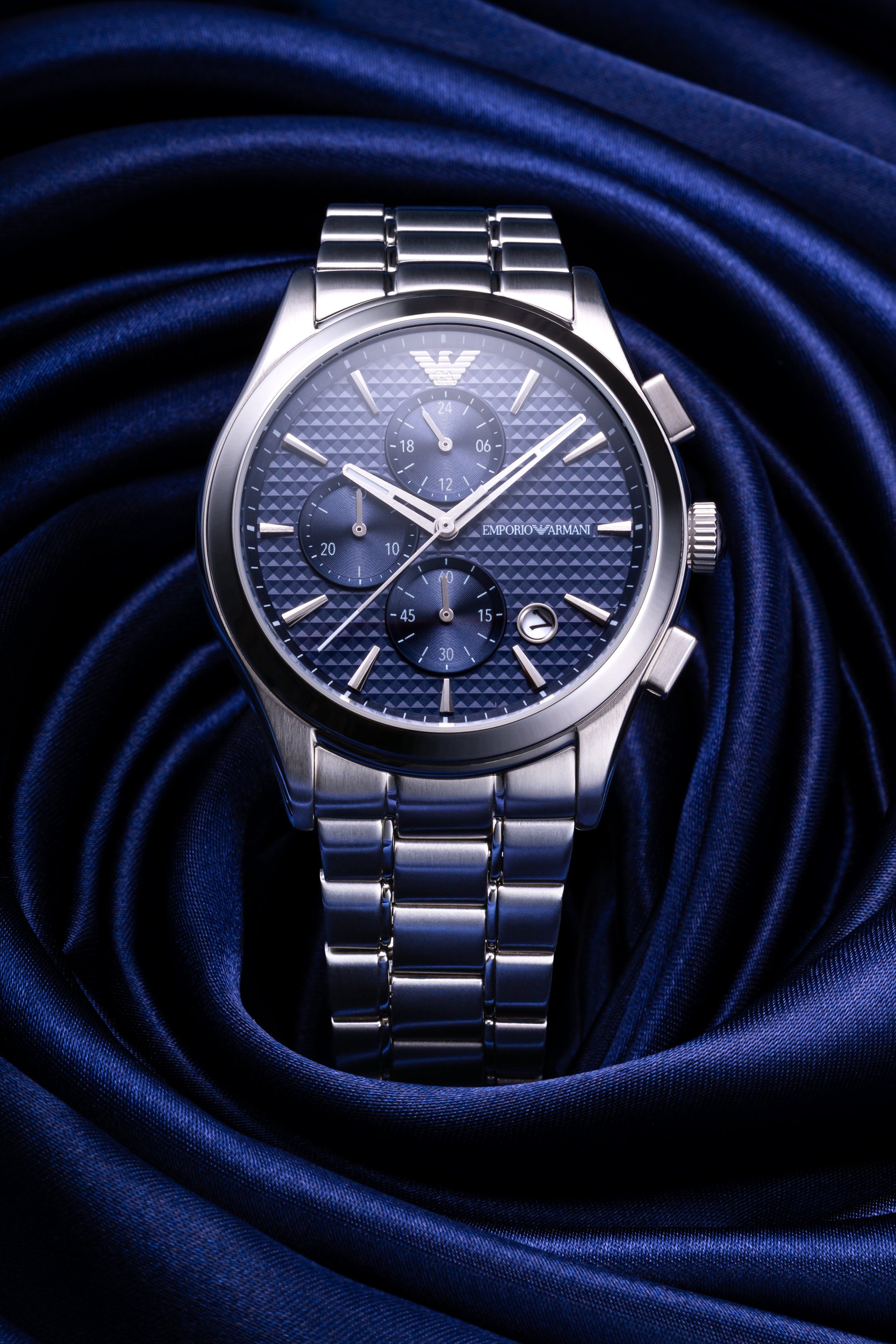 Creative watch product photograph of Emporia Armani watch sat on a navy silk cloth spun into a rosette knot.