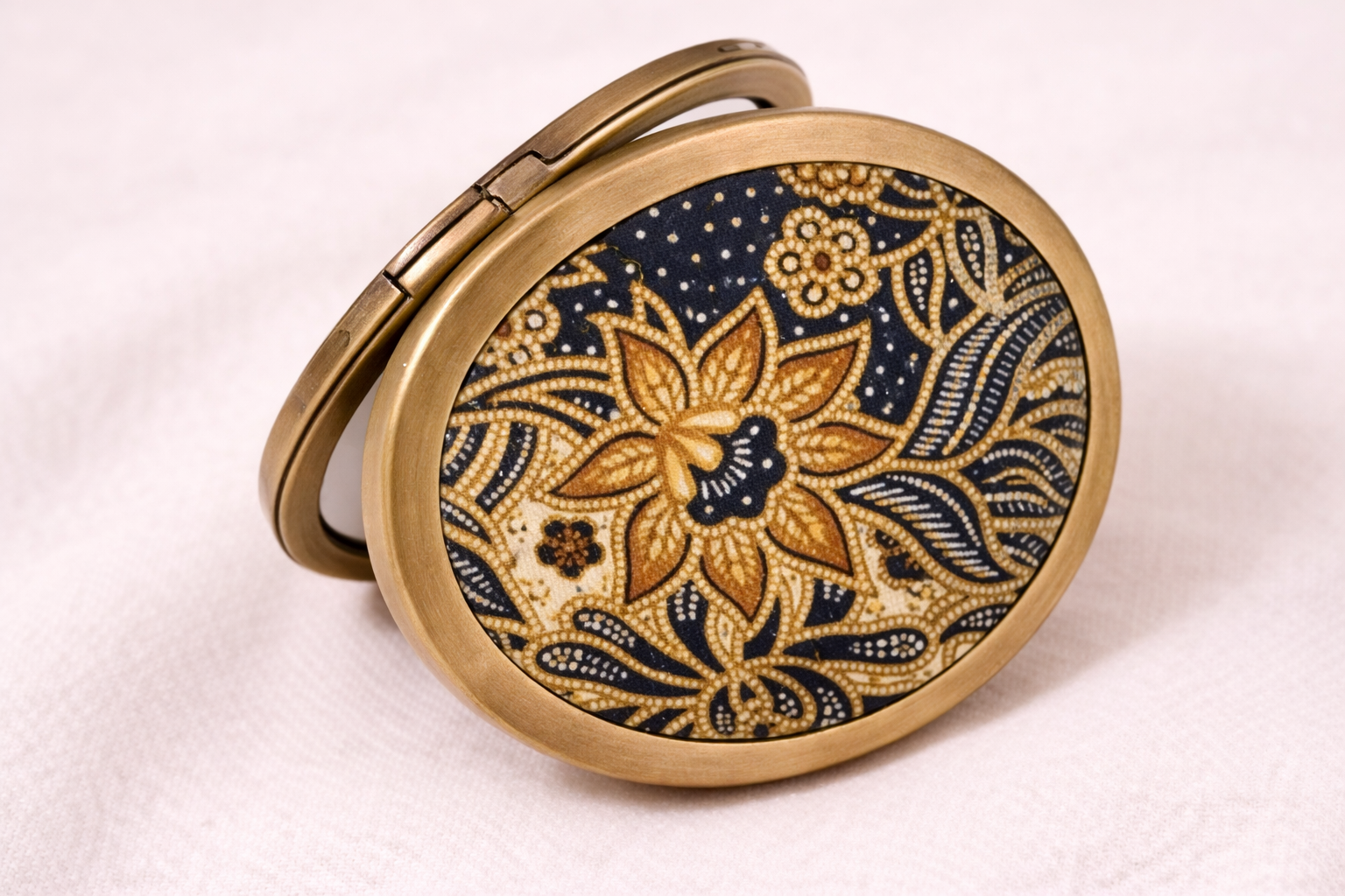 Batik-inspired compact mirror with gold floral design on a round case