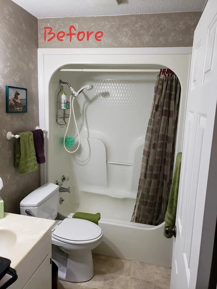 A small bathroom with a white bathtub/shower combination, shower curtain pulled to the side, a green cleaning sponge hanging from the showerhead, toilet with a green seat cover, and a countertop with a tissue box. There is a towel rack with green and purple towels, a framed picture on the wall, and a beige floor. "Before" is written in red text at the top of the image.