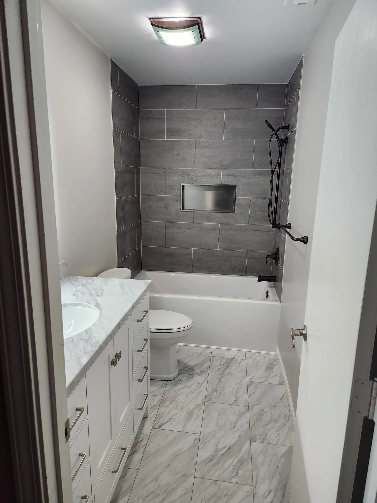 Bathroom with white vanity and marble countertop, toilet, and shower with gray tiles and built-in niche. Marble floor tiles.
