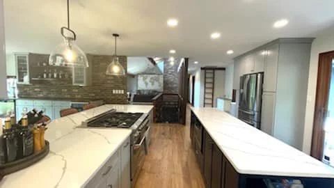 Modern kitchen with white marble countertops, stainless steel appliances, and pendant lighting.