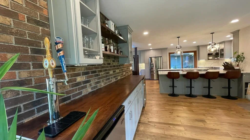 Modern kitchen with a brick wall, wooden countertop, bar-stool seating, stainless steel appliances, and pendant lighting.