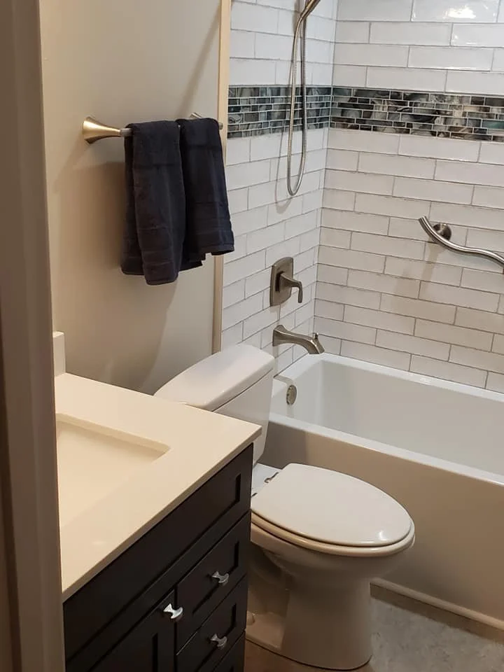 Bathroom with a bathtub, toilet, vanity with sink, and dark towels on a towel rack.