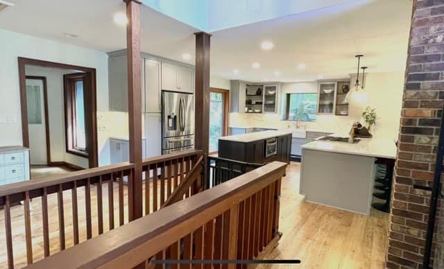 Modern kitchen and dining area with wooden staircase, stainless steel appliances, white cabinets, and granite countertops.