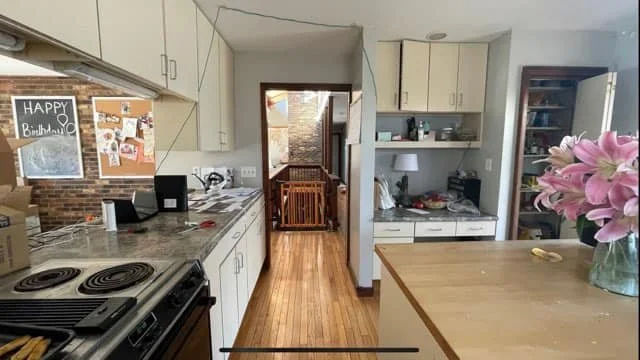 Kitchen with white cabinets, wooden flooring, a stove, a bulletin board, and a large flower arrangement on an island.