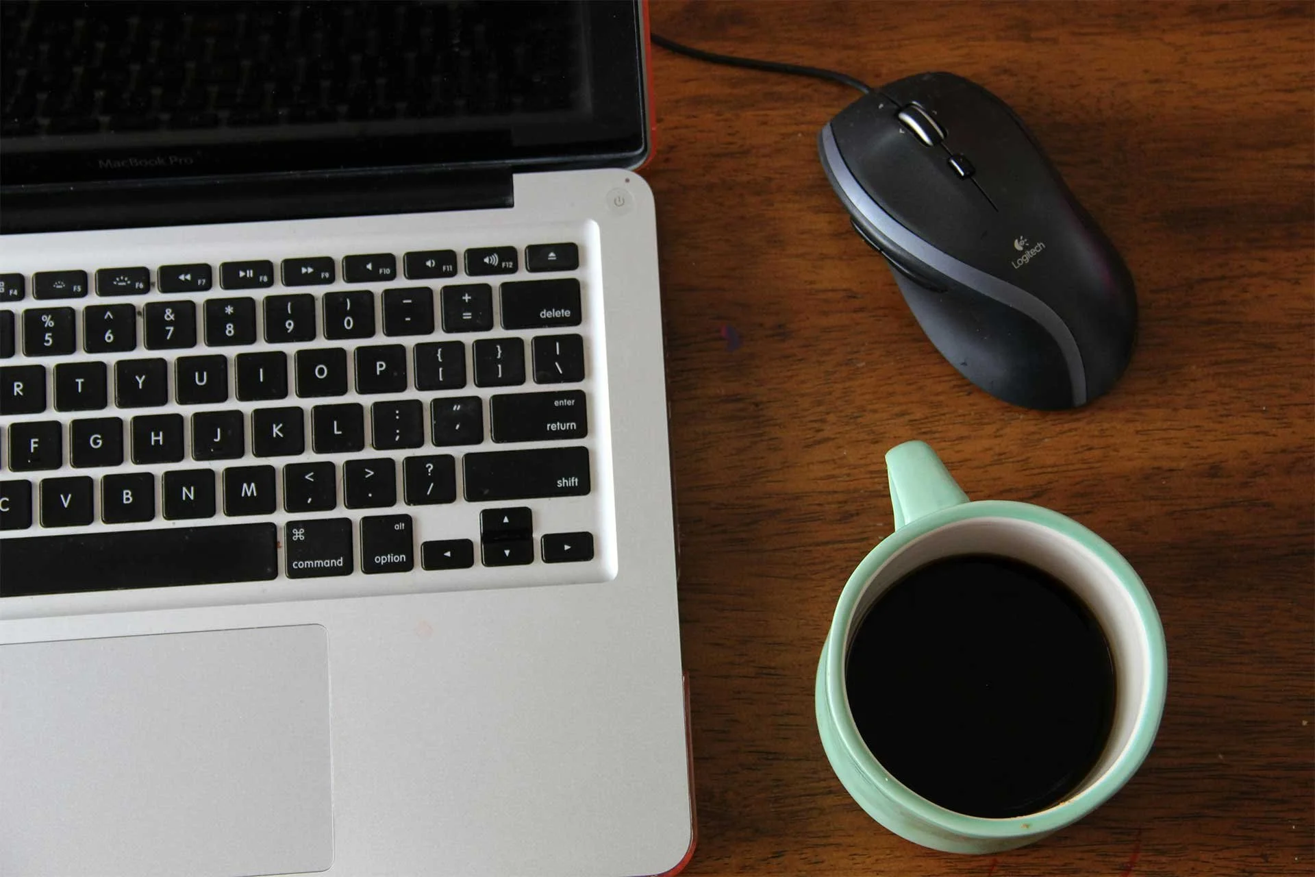 A mouse, a laptop keyboard, and a cup of coffee resting on a desk