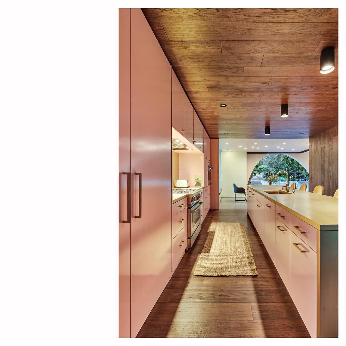 The &ldquo;wood womb&rdquo; (walls, ceiling and floor) of the kitchen in the El Sereno Residence by @hsumccullough compliment the pink cabinets and brass island and backsplash. The dining room, kitchen and living room combine to create a 60 feet long