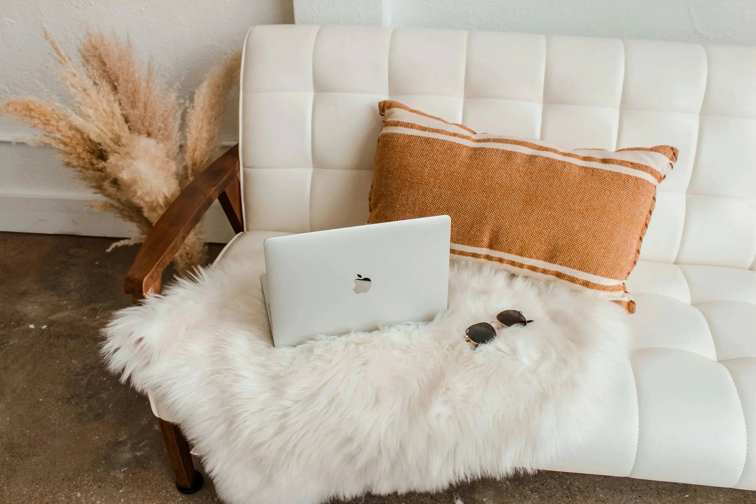 An apple computer, sunglasses and pillow sitting on top of a white couch