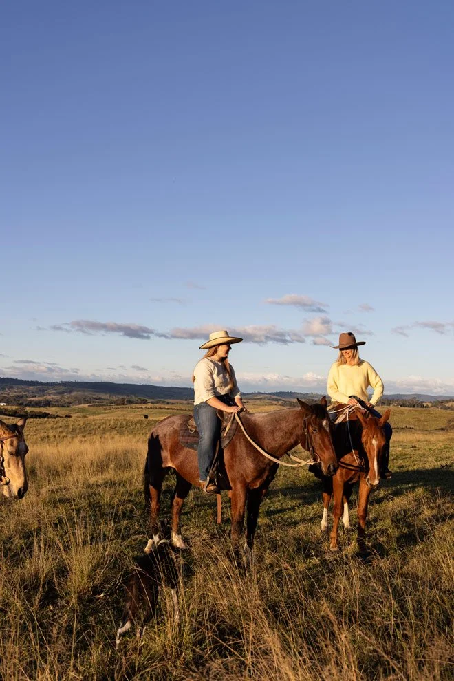 Brand photography Bega Valley, Sophie and Gen of Reins to Resilience on horseback across open grasslands at golden hour, Candelo NSW