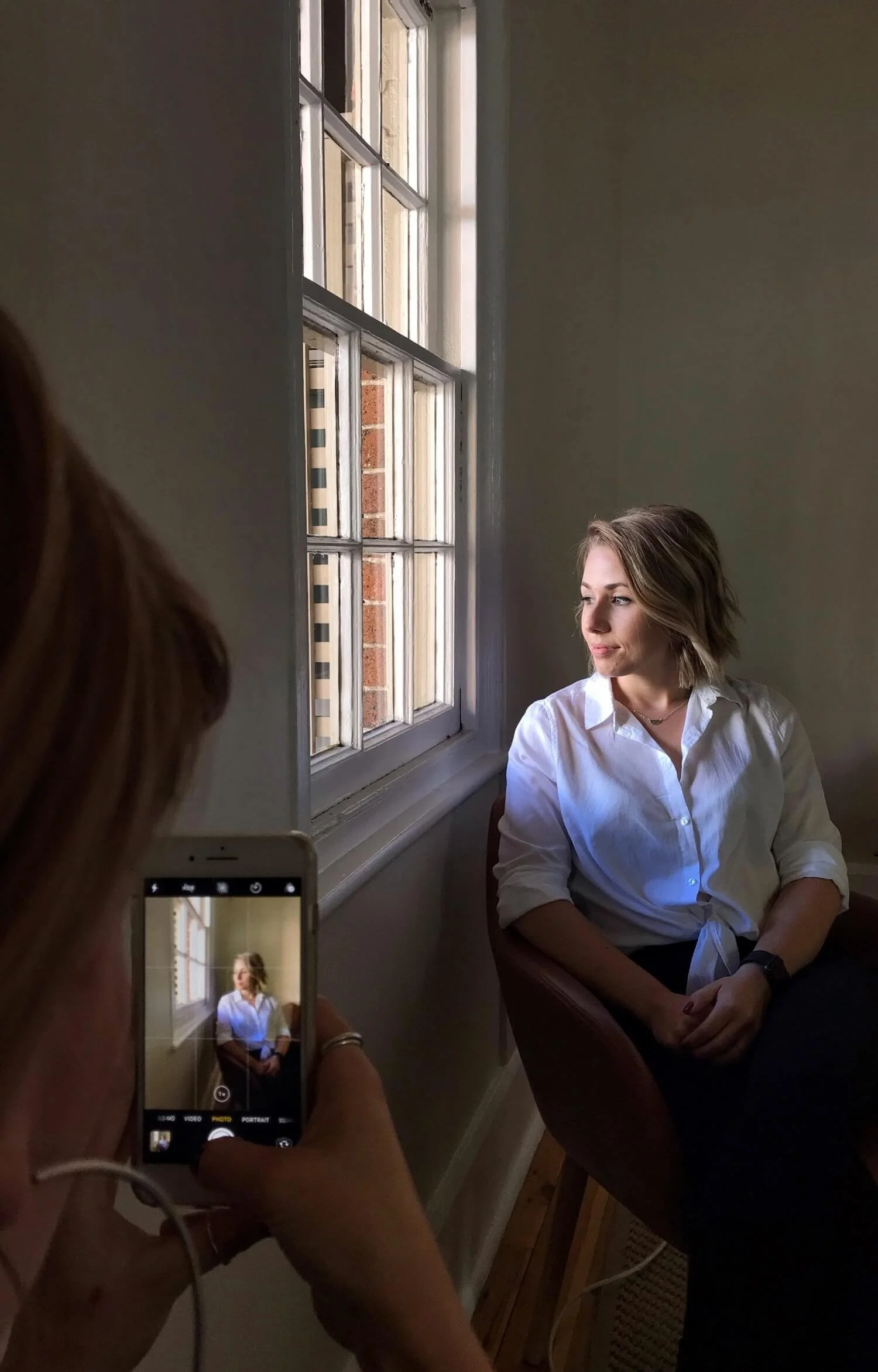 Workshop participant taking a portrait of a woman using natural window light during a phone photography workshop for small business owners.