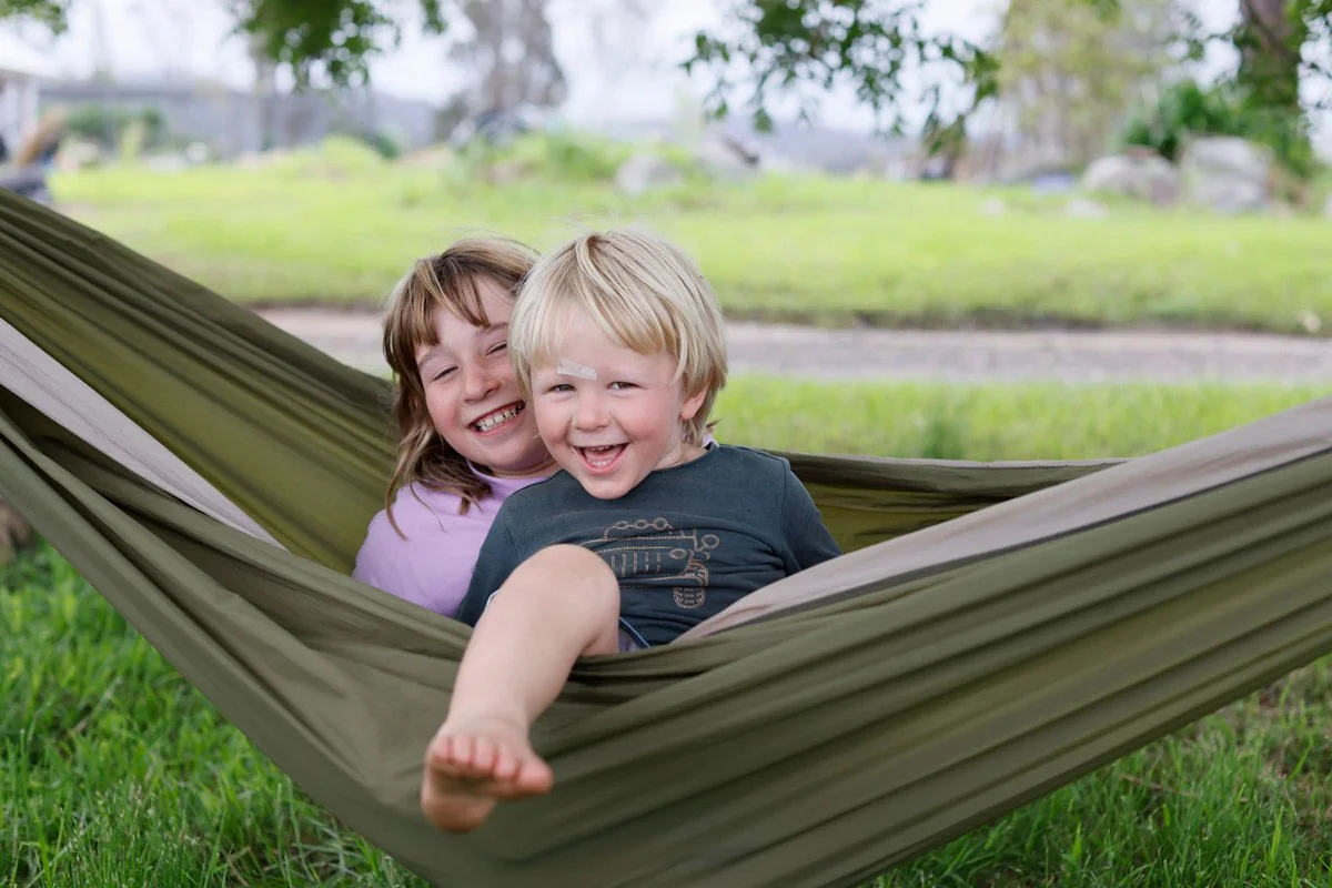 Siblings playing in hammock during summer under a tree, photographed as a quiet moment of mindfulness in everyday life.