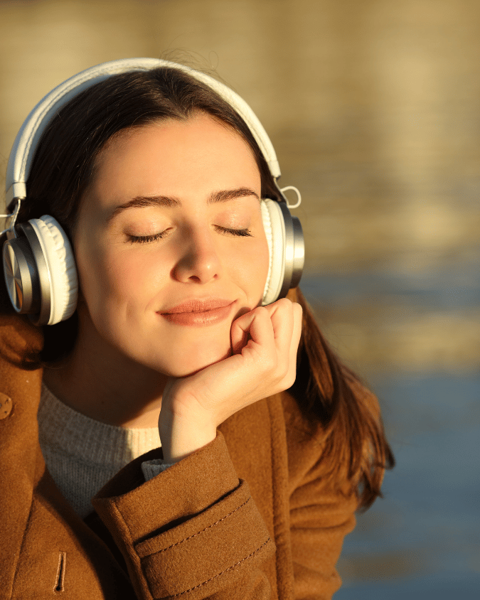 A woman wearing headphones and smiling with her eyes closed