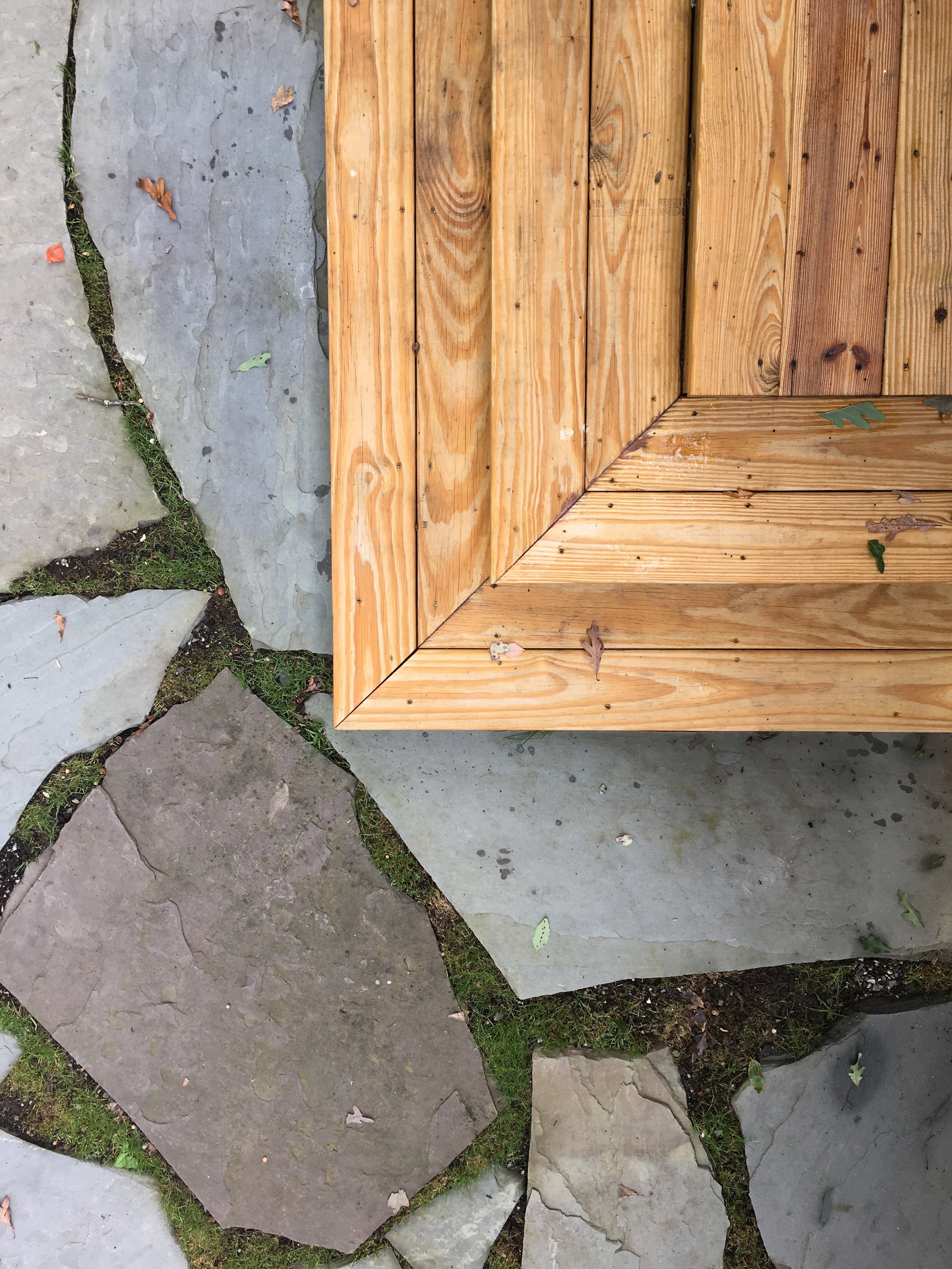 Corner of a wooden structure on top of stone paving stones with small patches of grass and fallen leaves.