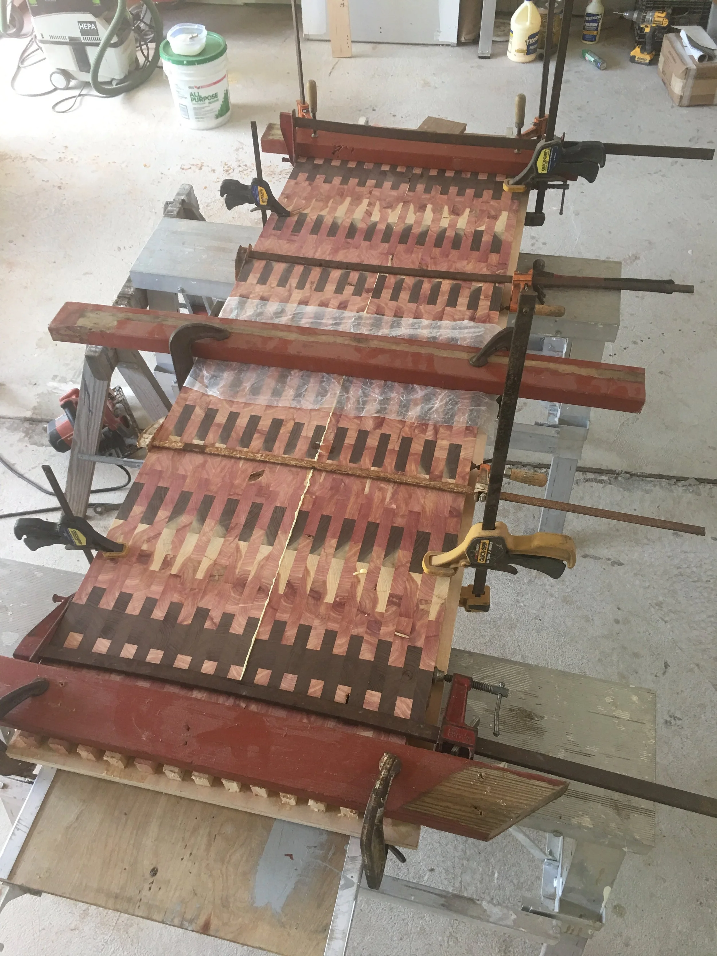 Clamps holding together a woodworking project with wooden slats on a workbench in a workshop.