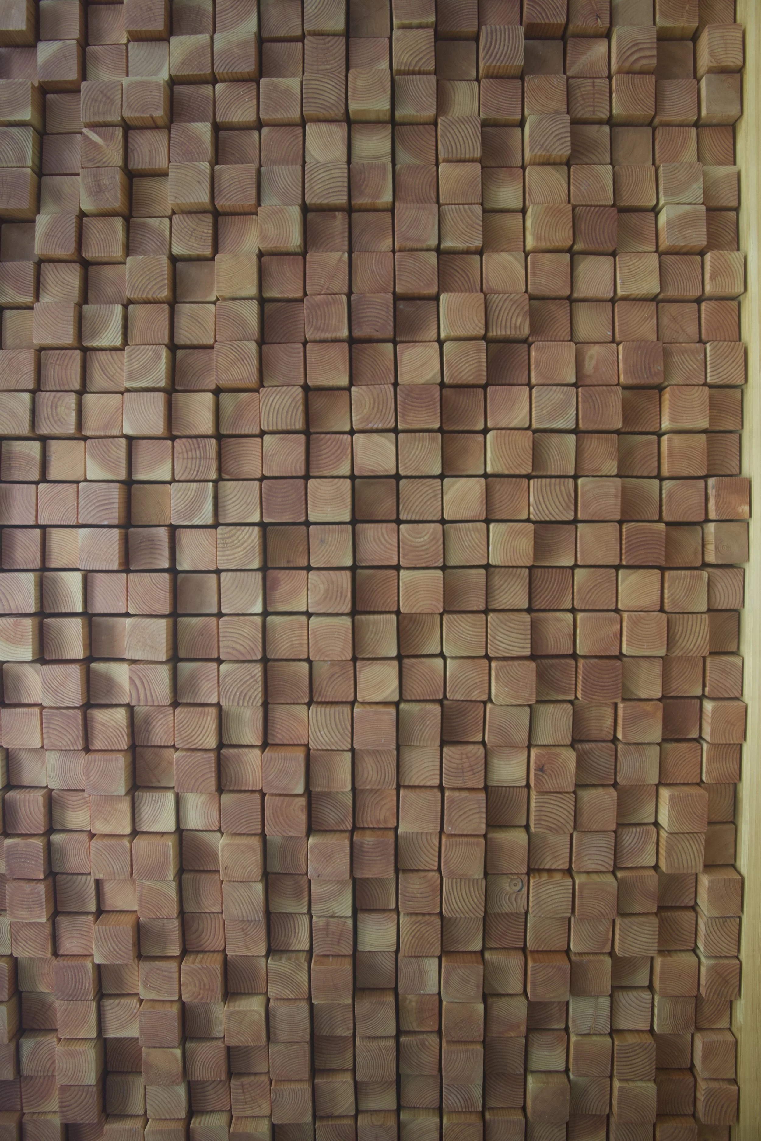 A wall of neatly stacked wooden blocks or planks, arranged in a grid pattern.