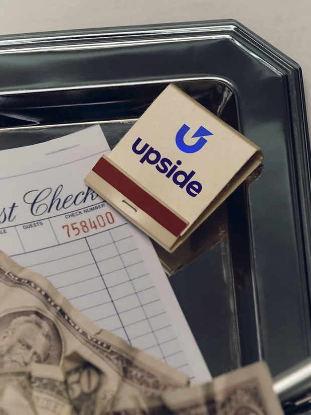 matchbook with a blue logo for upside on a metal tray with a paper check and a dollar bill in the corner