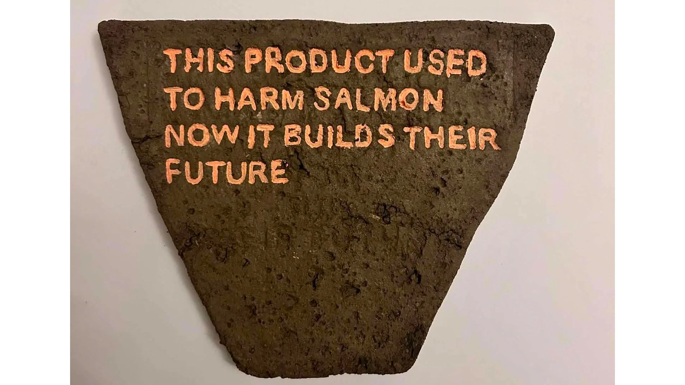 Final composting tile with painted lettering, made from reclaimed sea-lice composite material.