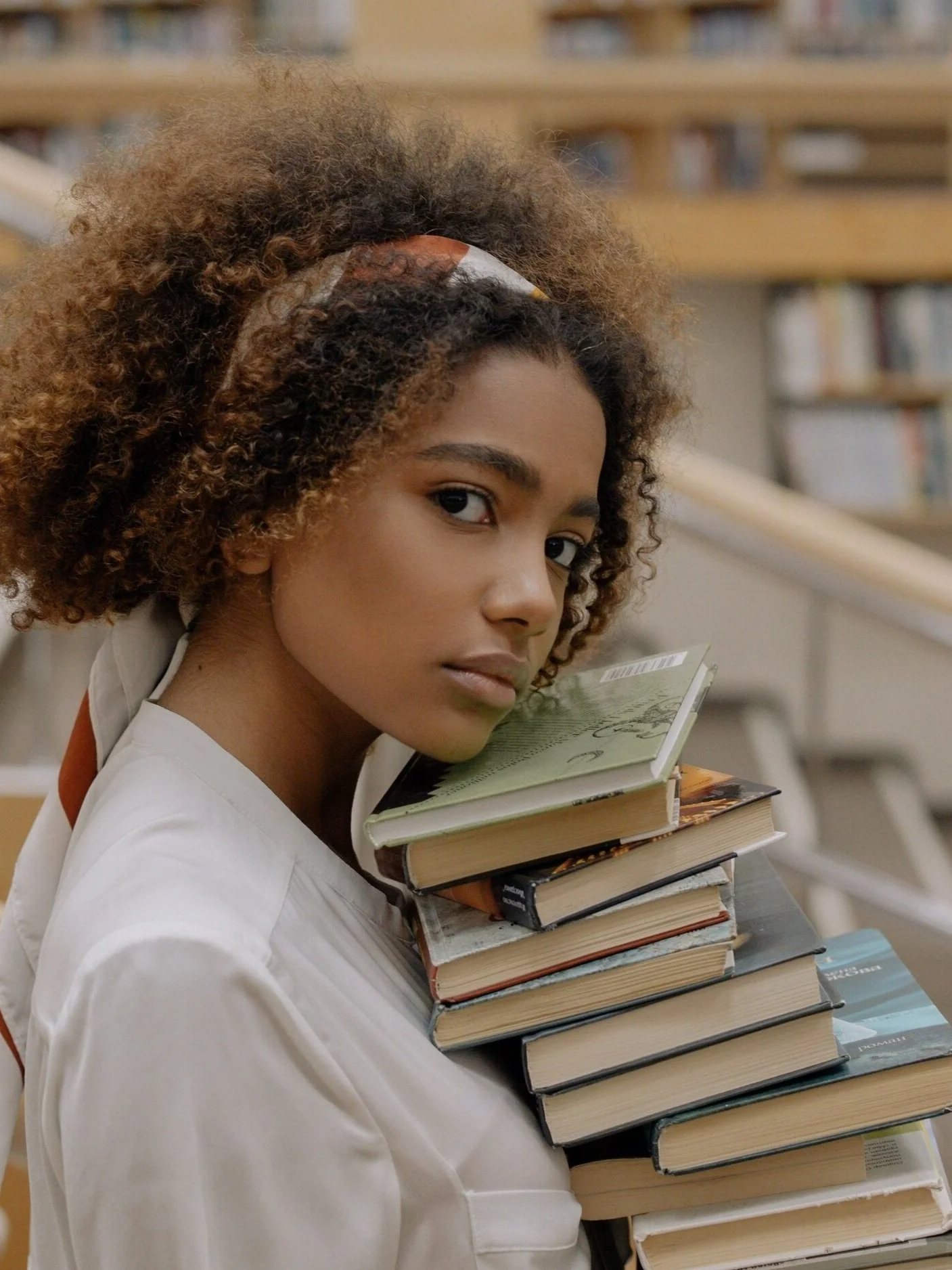Young black woman with afro and striped bandana headband wearing white tshirt carrying large stack of library books