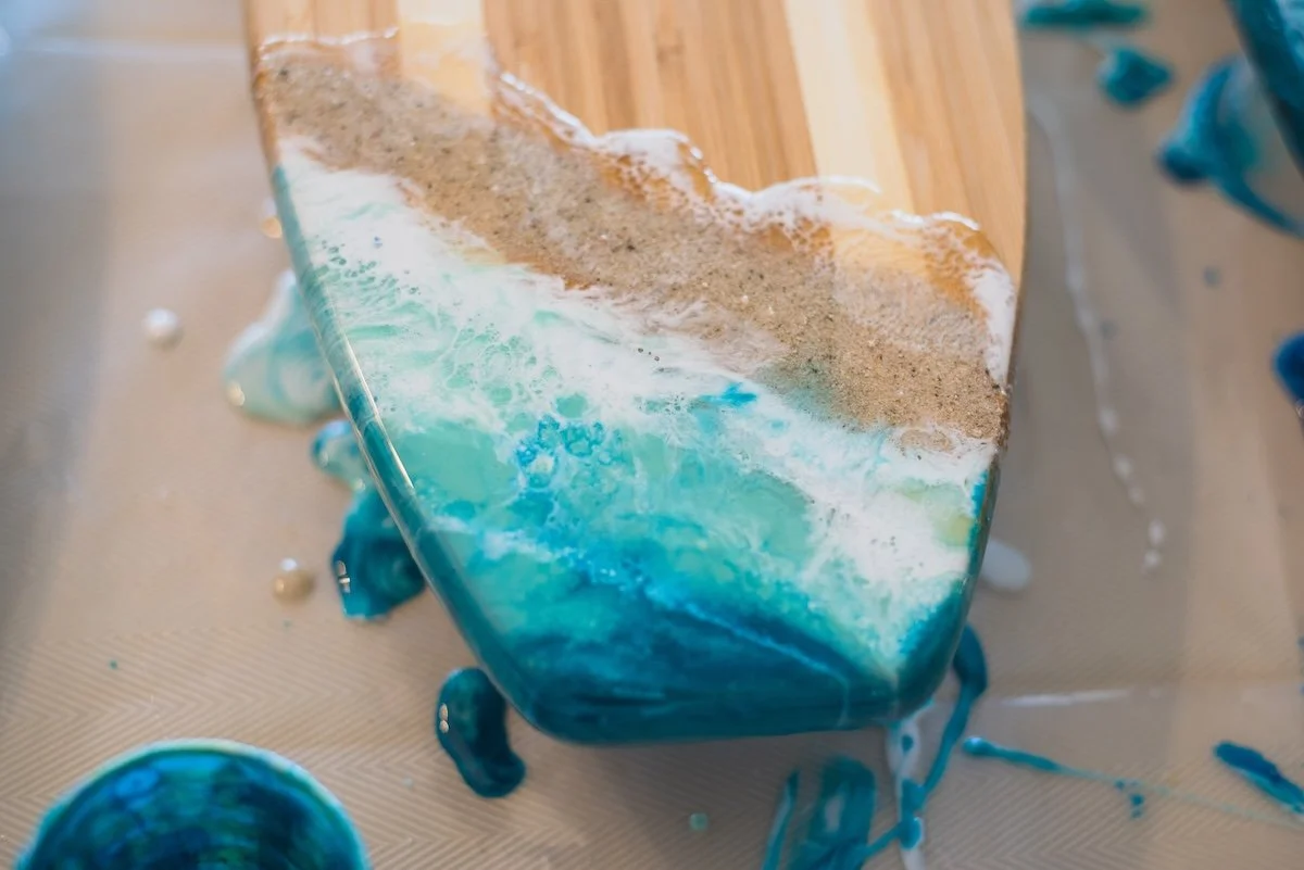 A piece of wood with a colorful ocean-themed resin river flowing through it, with blue, white, and brown colors, and some spilled resin around