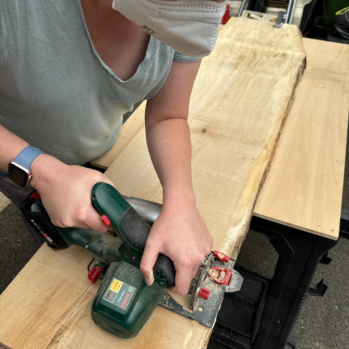 Person using a battery-powered handheld planer to plane a large wooden board on a workbench.