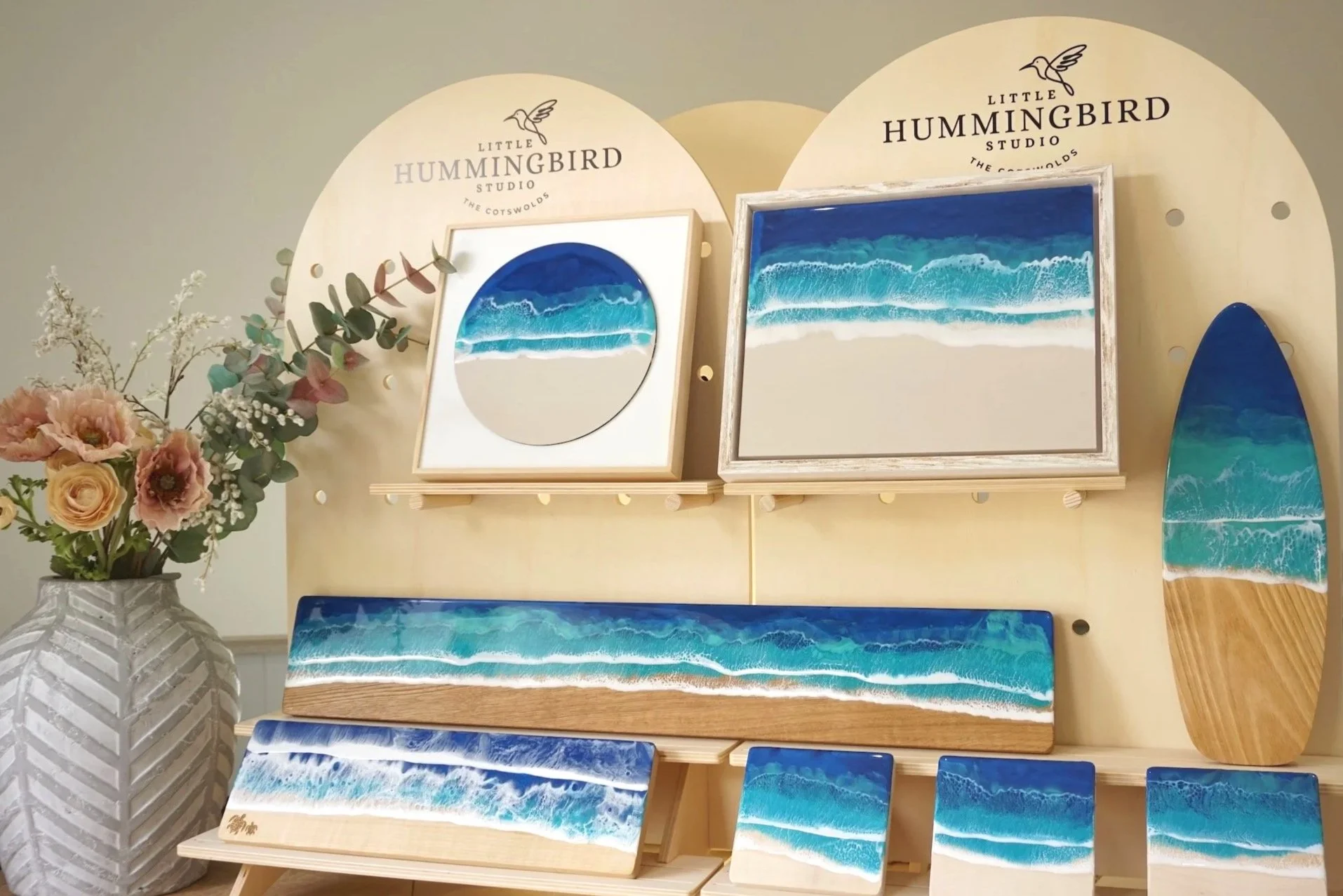 Various ocean-themed resin artworks on display at Little Hummingbird Studio, with floral arrangement in a white vase in the foreground.
