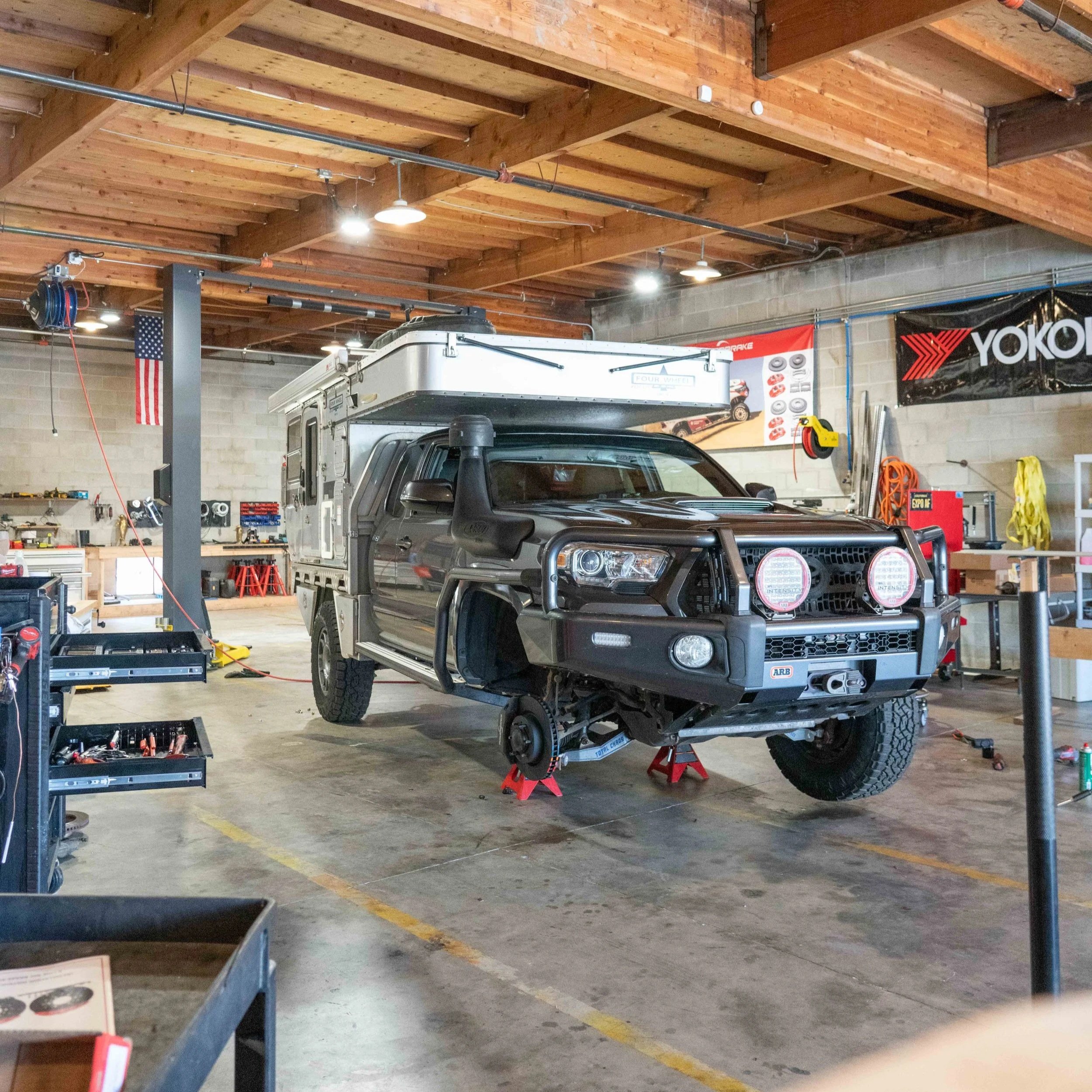 A garage with a wooden ceiling and walls, a black pickup truck on jack stands, and various tools and equipment.