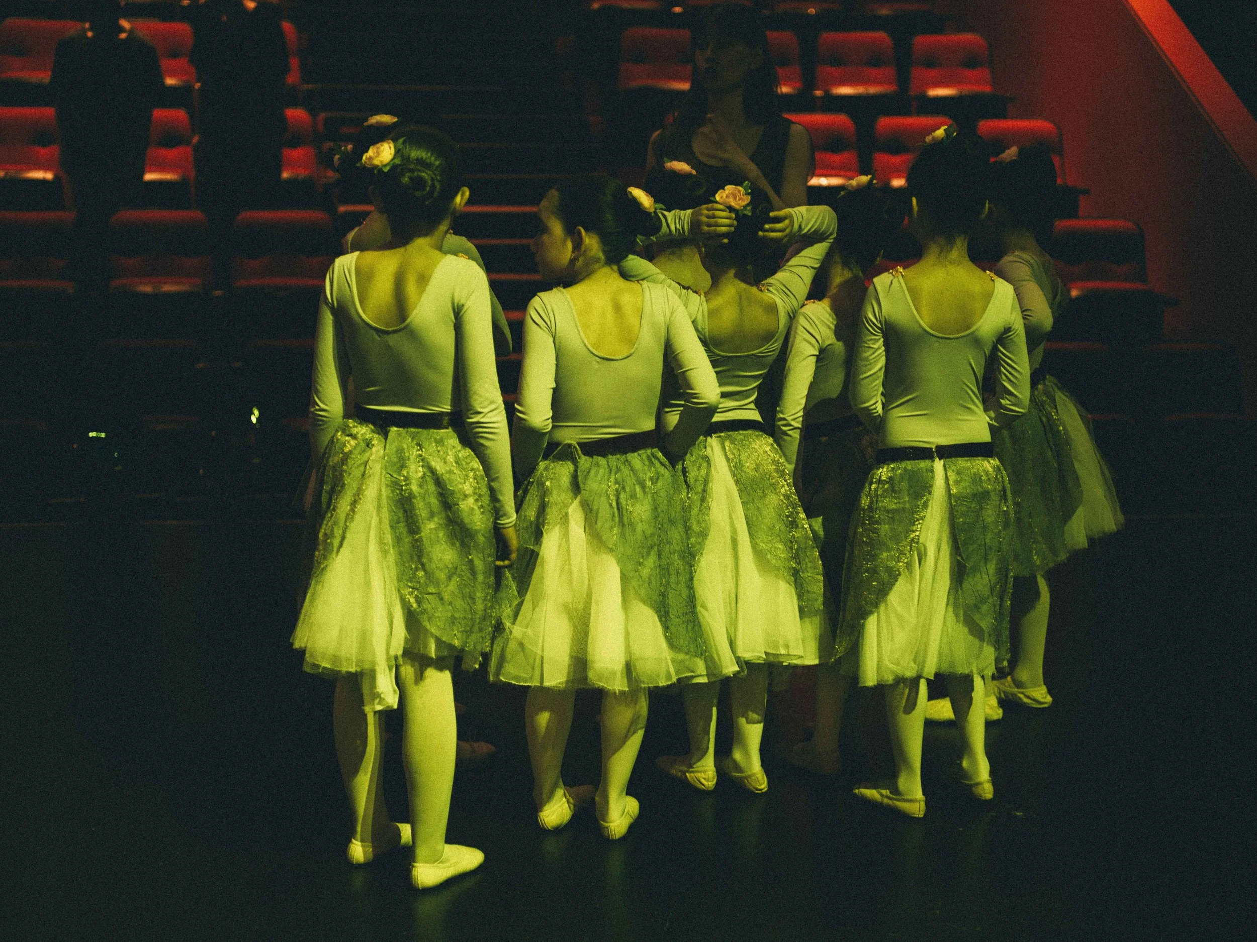 Ballet dancers in green and white costumes backstage in a theater, preparing for a performance.