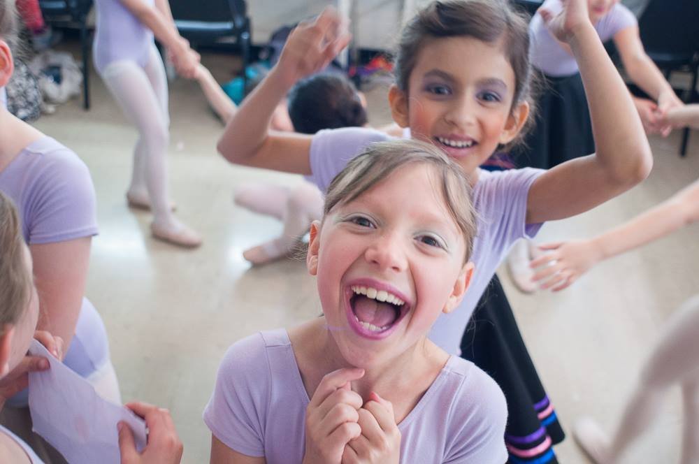 Smiling young girls in ballet class, joyfully posing and wearing ballet leotards and tights.