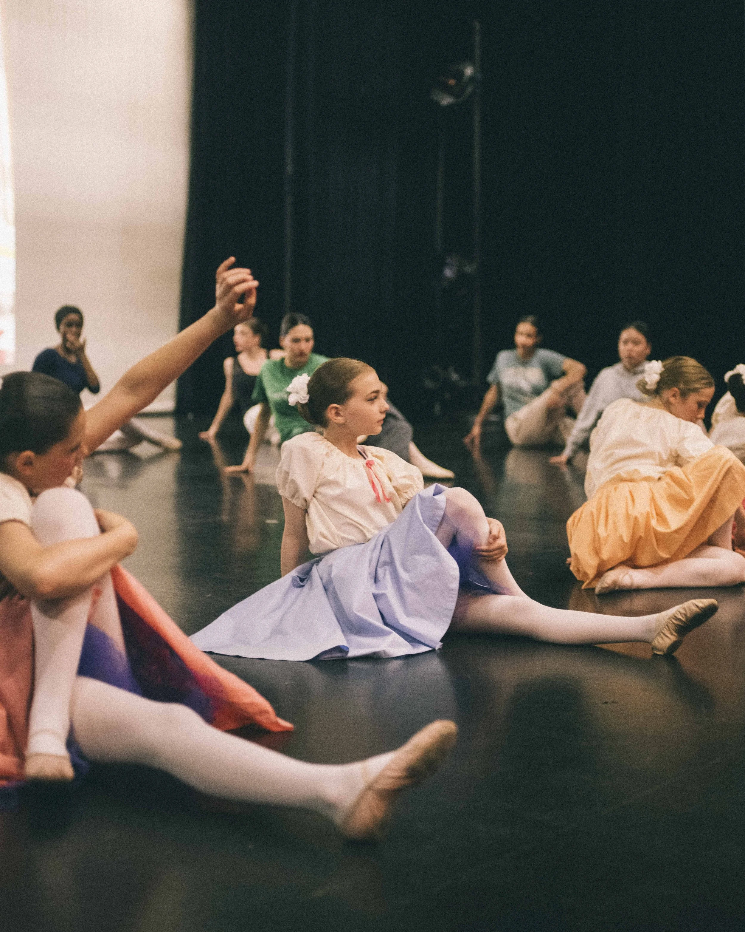 Young girls rehearsing ballet stretches on stage during dance practice.