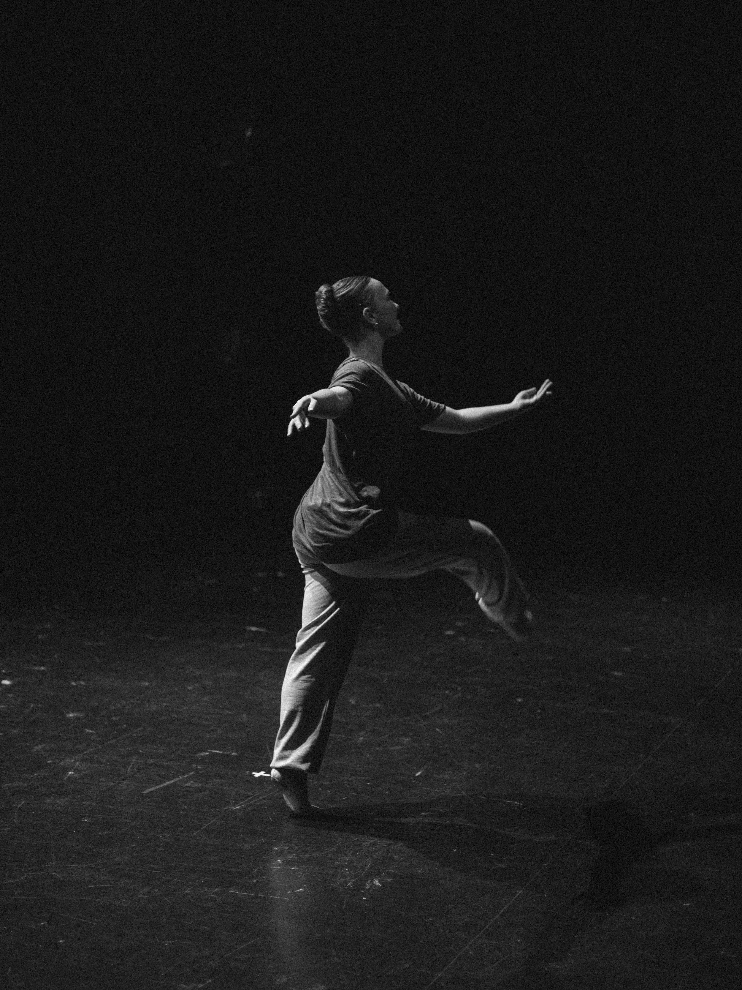 A woman performing a dance pose on stage in a dark setting, illuminated by stage lighting.