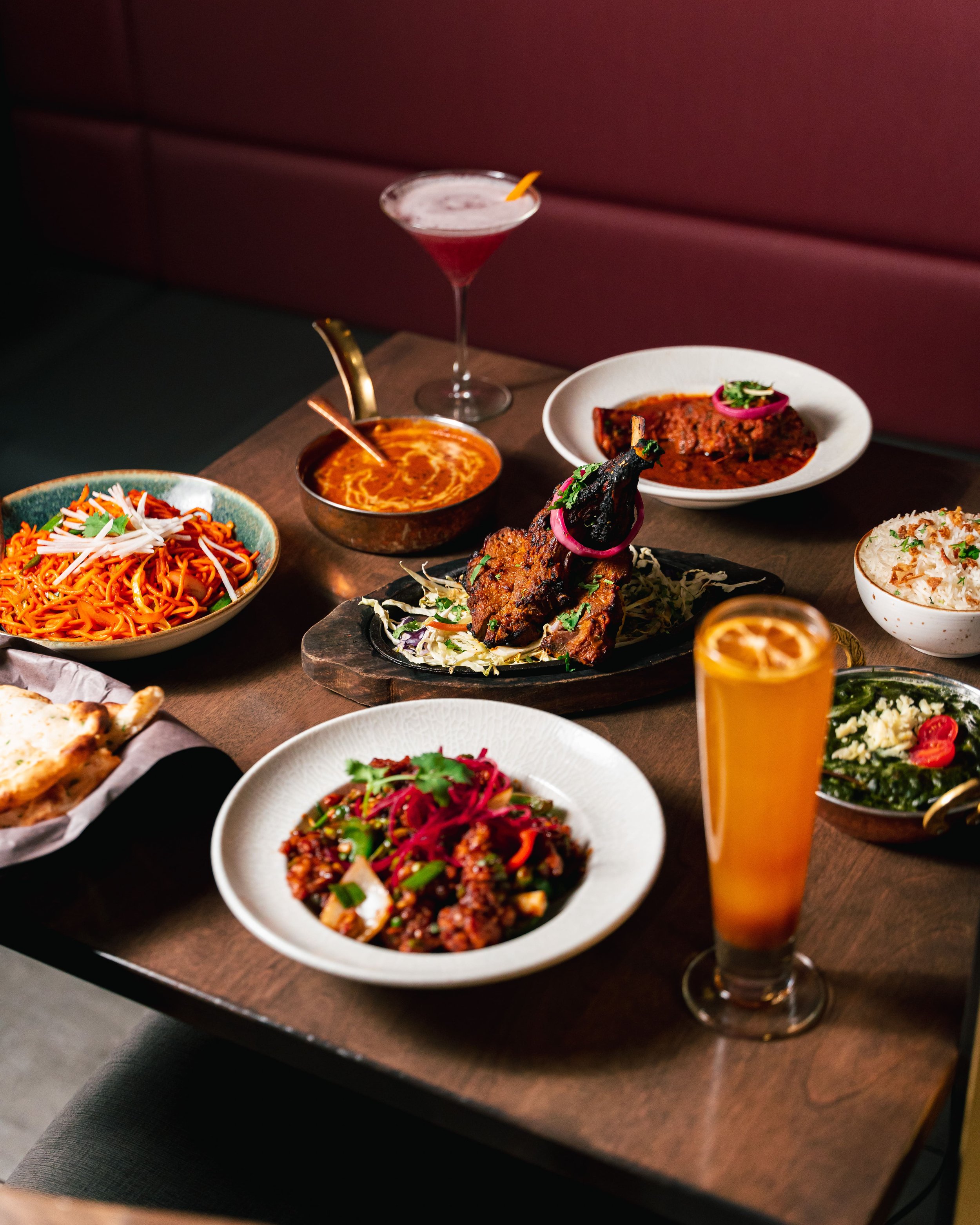 An indulgent table spread showcasing vibrant curries, sizzling tandoor specialties, and handcrafted drinks, thoughtfully plated for a refined dining experience.