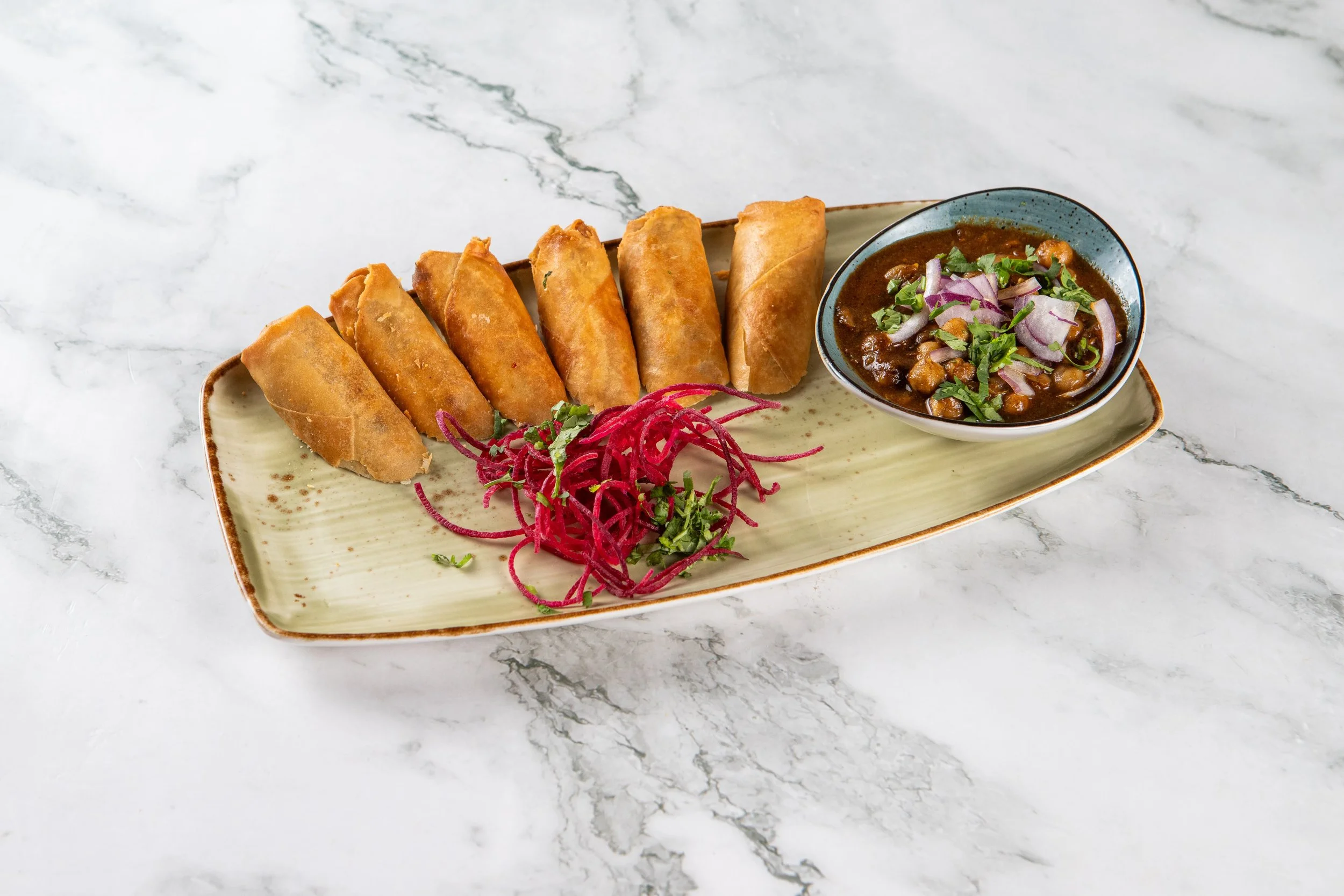 Samosa Rolls (Veg): Spiced potatoes and peas in a crispy pastry wrapper. Served with chana masala and chutneys.