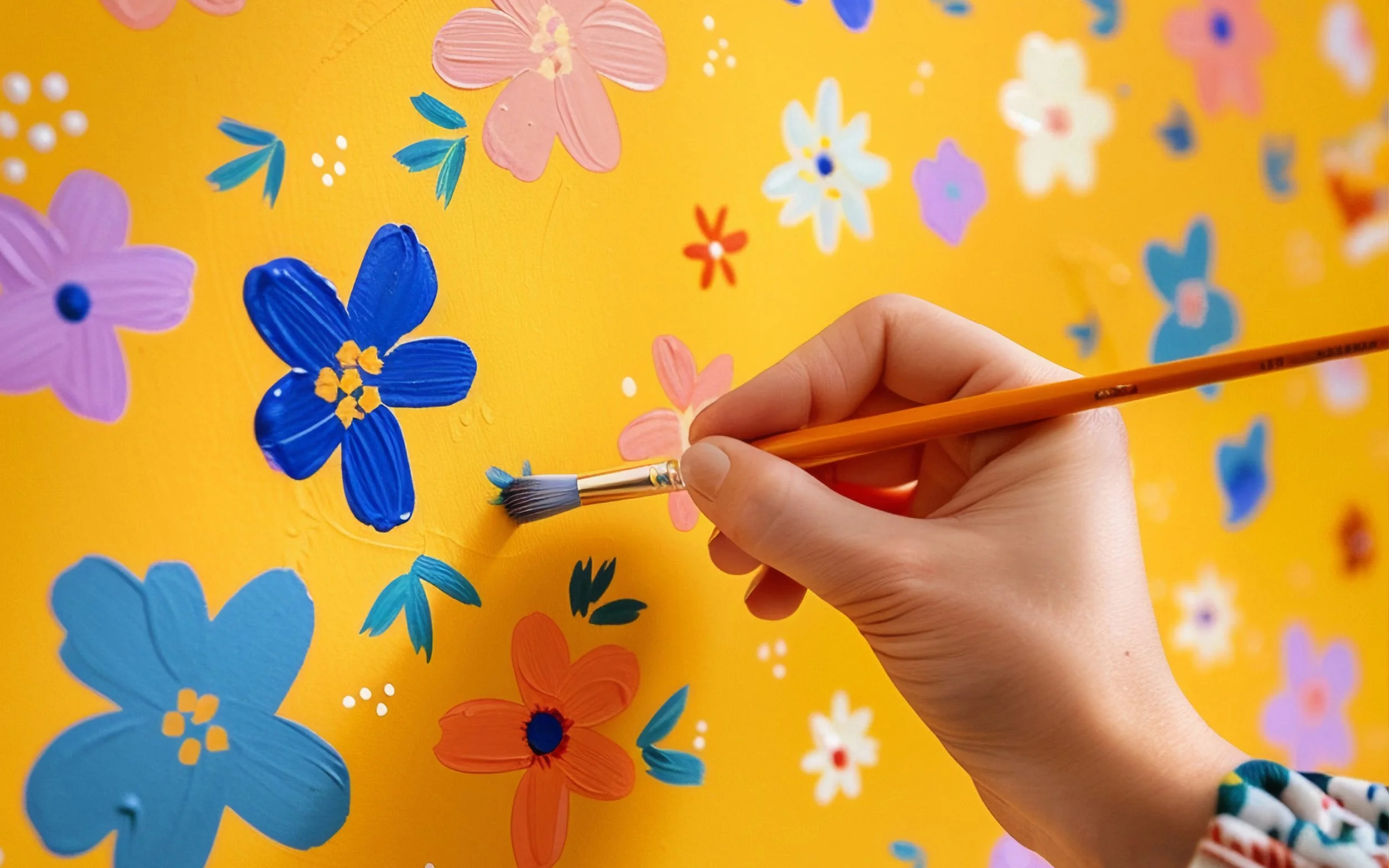 A person's hand holding a paint brush painting flowers