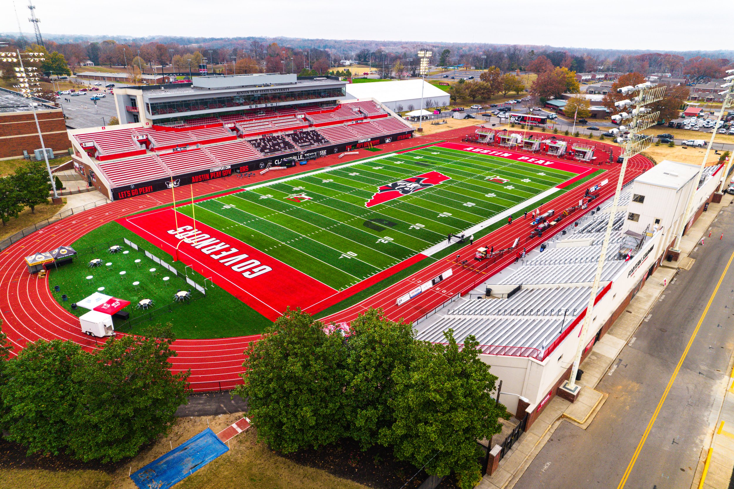 Aerial view of a football stadium with red and green turf, surrounded by bleachers; featuring a running track and empty seating areas.