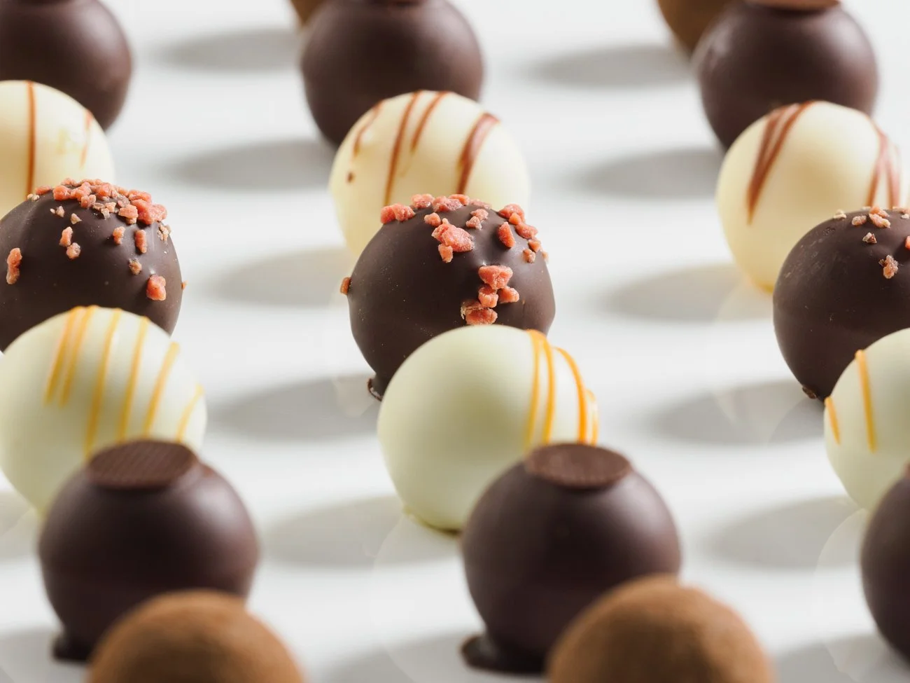 Assorted gourmet chocolate truffles on a white surface, with various toppings and decorations.