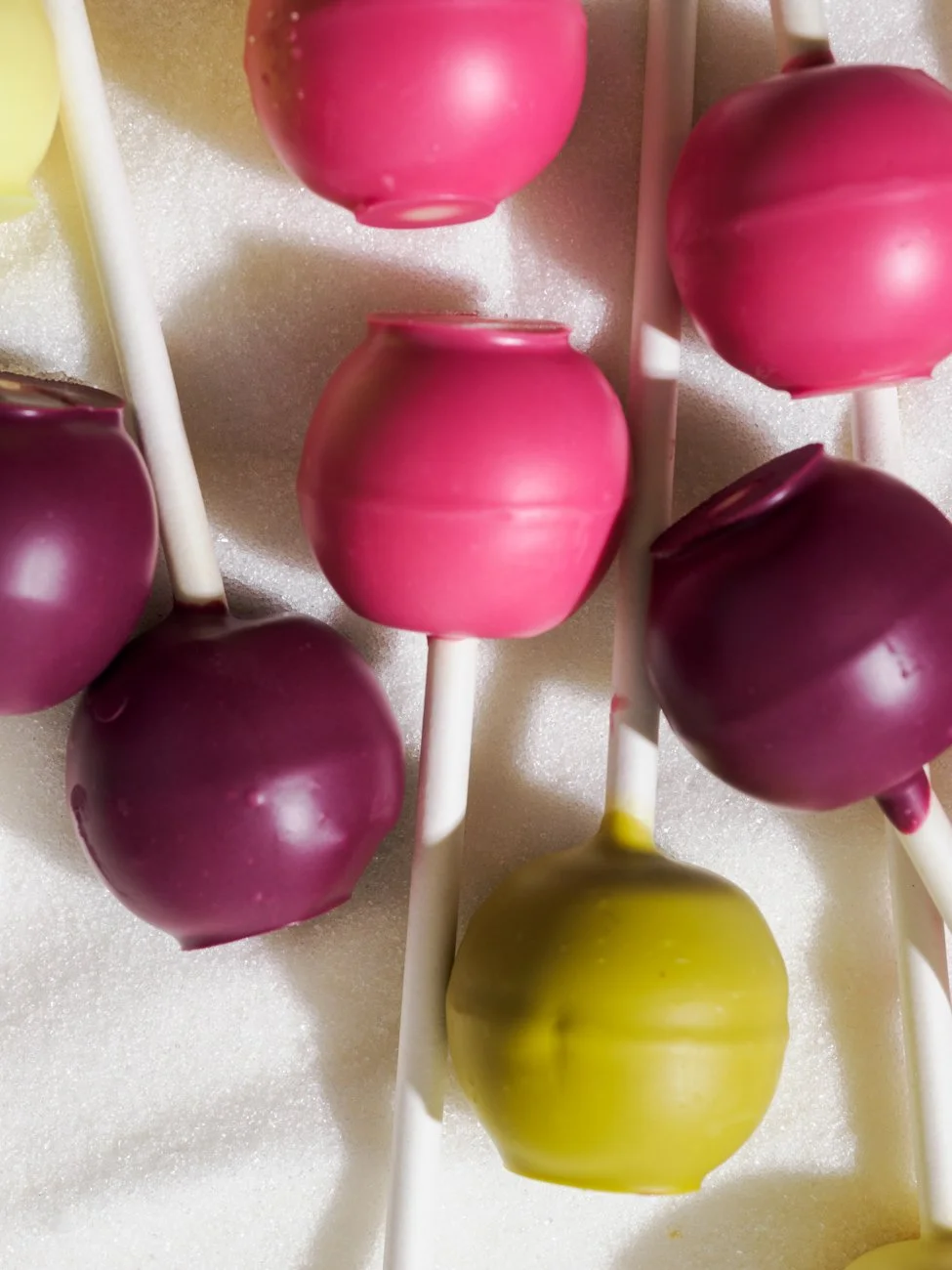 Colorful spherical candies on white sticks, arranged on foam background, in pink, purple, and yellow colors.