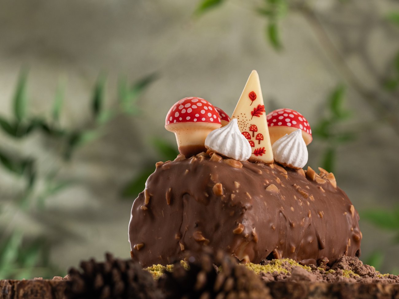 Chocolate dessert decorated with red and white mushroom-shaped candies, white meringue kisses, and a white chocolate piece with red leaf and mushroom designs.